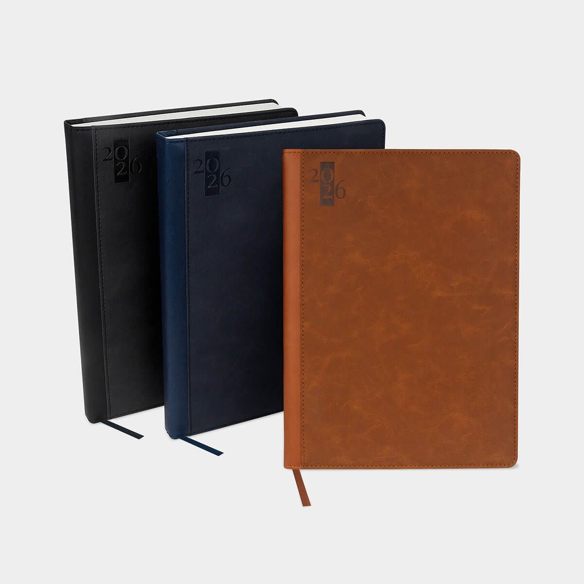 Tres cuadernos de color negro, azul oscuro y beige dispuestos en fila sobre un fondo gris claro.