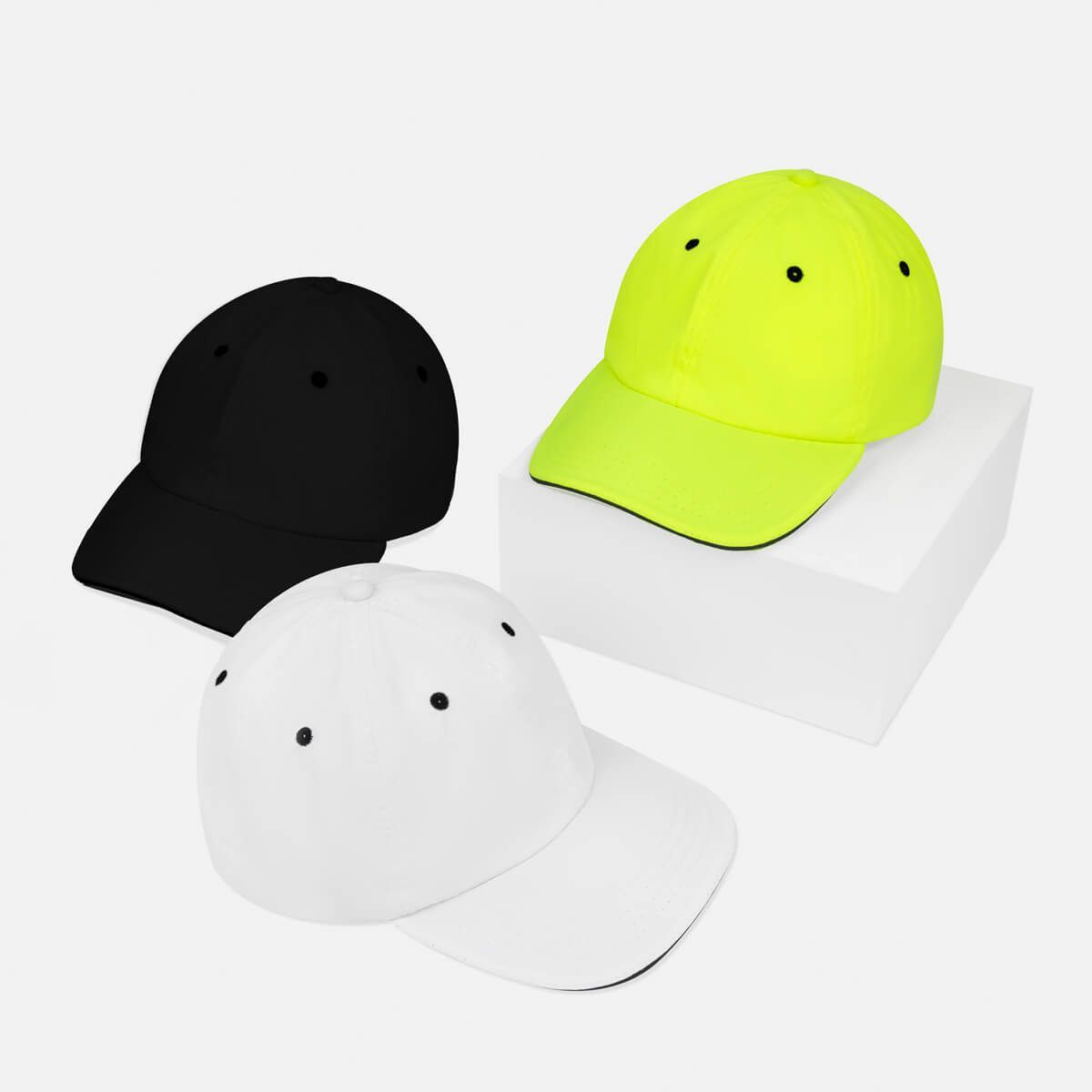 Tres gorras de béisbol en negro, blanco y amarillo neón dispuestas sobre un fondo blanco.