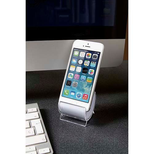 Un teléfono inteligente blanco reposa sobre un soporte de acrílico transparente en un escritorio oscuro, colocado frente a la pantalla y el teclado de una computadora.