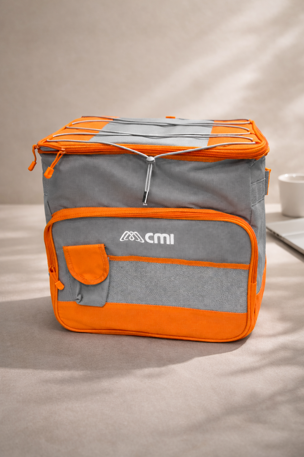 Una bolsa térmica isotérmica de color naranja y gris, con un bolsillo frontal y un cordón elástico en la tapa superior, colocada sobre una superficie neutra.