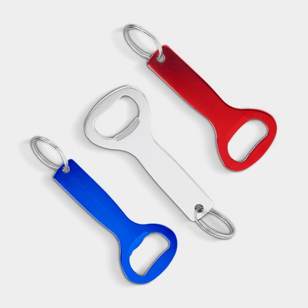 Tres llaveros abrebotellas de color rojo, blanco y azul, dispuestos en diagonal sobre un fondo gris claro liso.