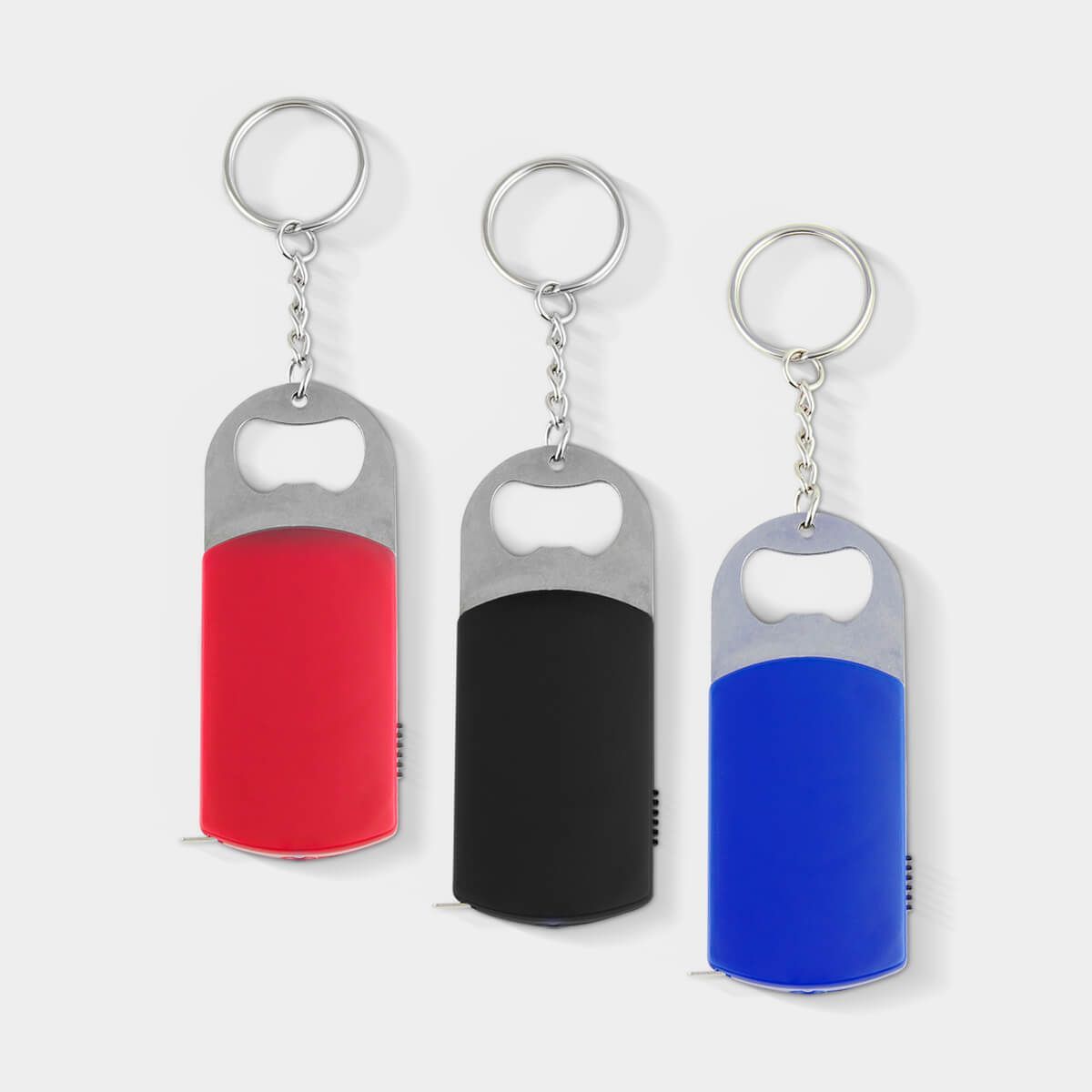 Tres llaveros abrebotellas de color rojo, negro y azul, dispuestos uno al lado del otro sobre un fondo blanco liso.