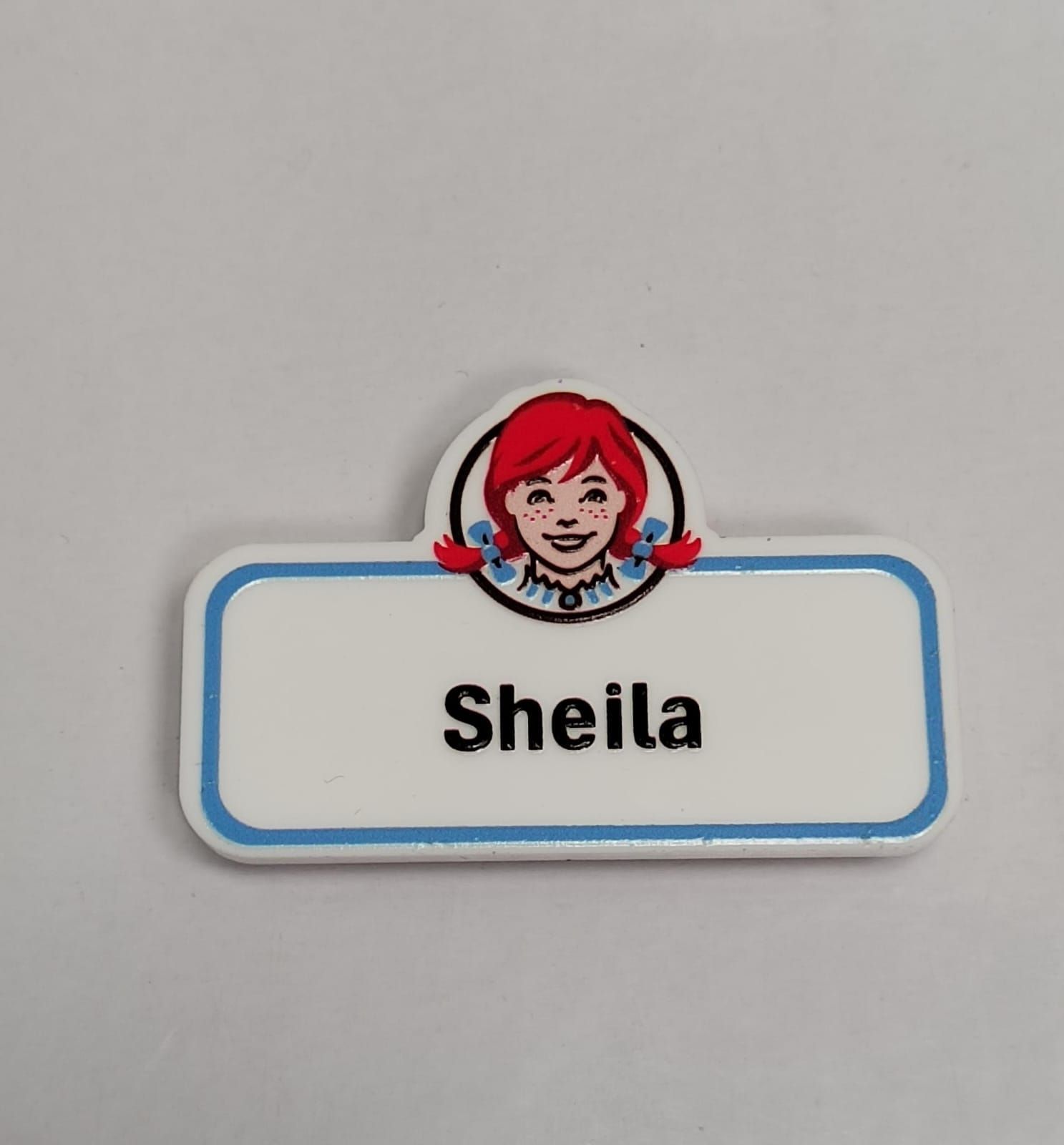 Una etiqueta blanca rectangular de Wendy's con un borde azul y el logotipo de Wendy's, que muestra el nombre 