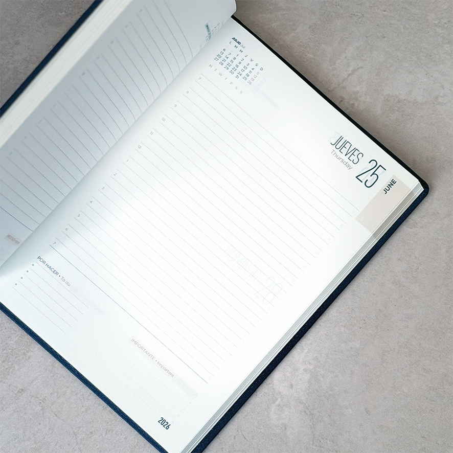 Una agenda abierta sobre una superficie gris, que muestra la fecha Jueves 25 con espacio para notas y un pequeño calendario.