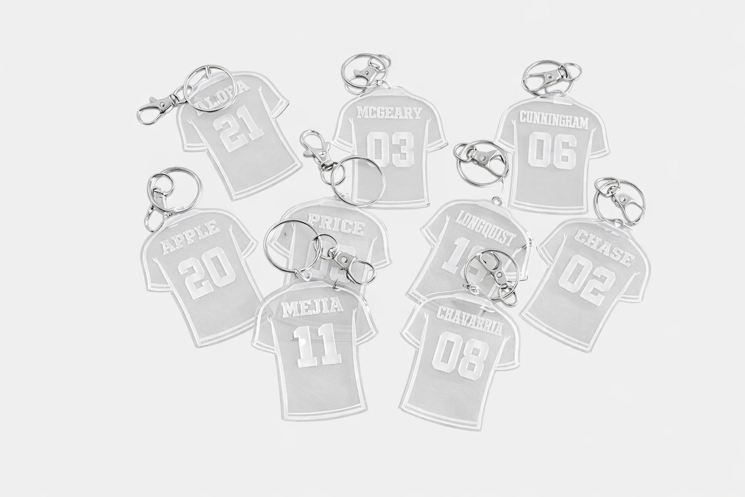 Una colección de llaveros de acrílico blanco con forma de camiseta, cada uno con un nombre y un número diferentes impresos.