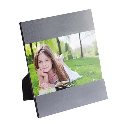 Un marco de fotos negro para escritorio, colocado sobre una superficie, muestra la foto de una persona descansando en un parque con césped.
