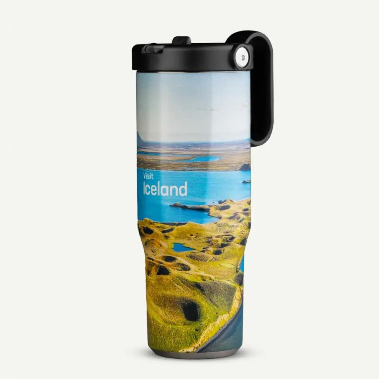 Un vaso térmico de viaje con una fotografía de un paisaje de Islandia, con agua azul brillante y colinas verdes, rematado con una tapa negra.