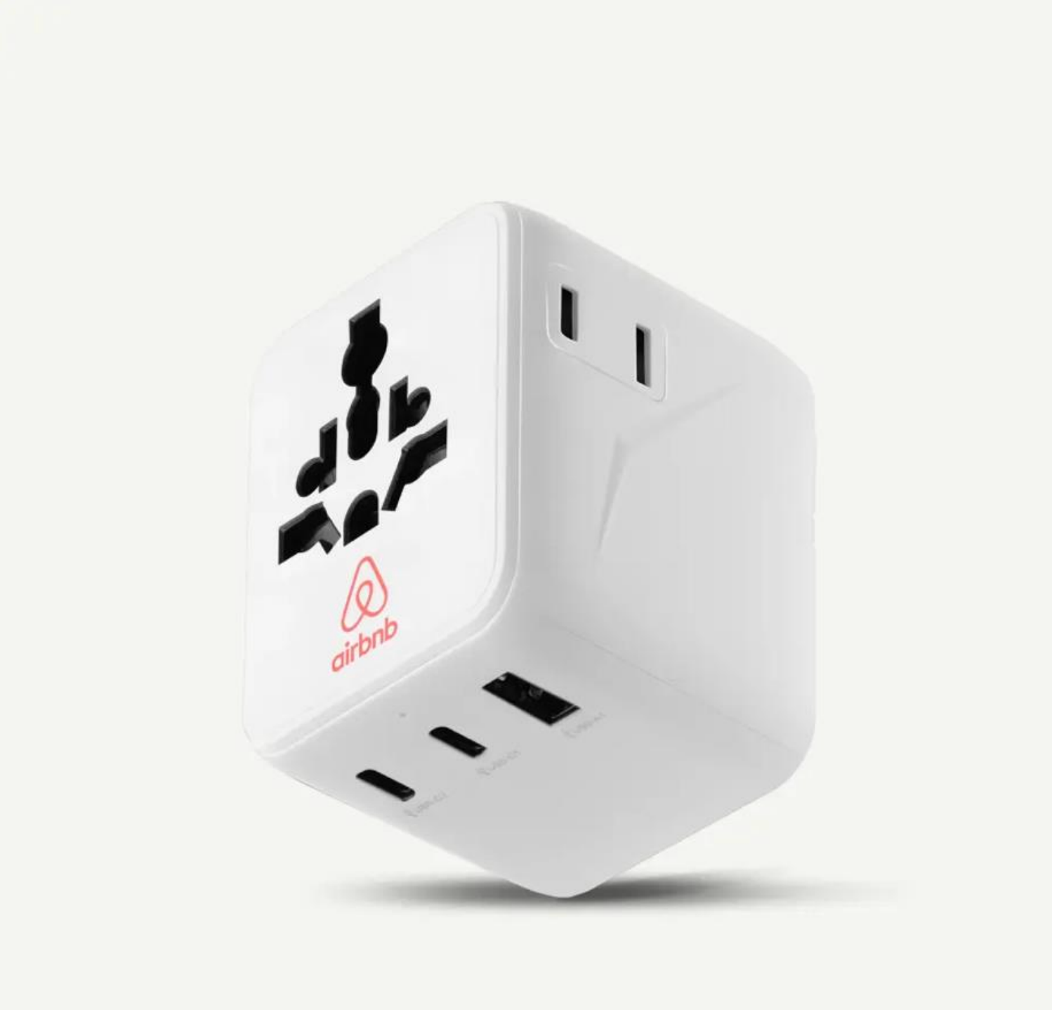 Un adaptador de corriente universal de viaje, blanco y cúbico, con el logotipo rojo de Airbnb, múltiples puertos de enchufe y ranuras USB.