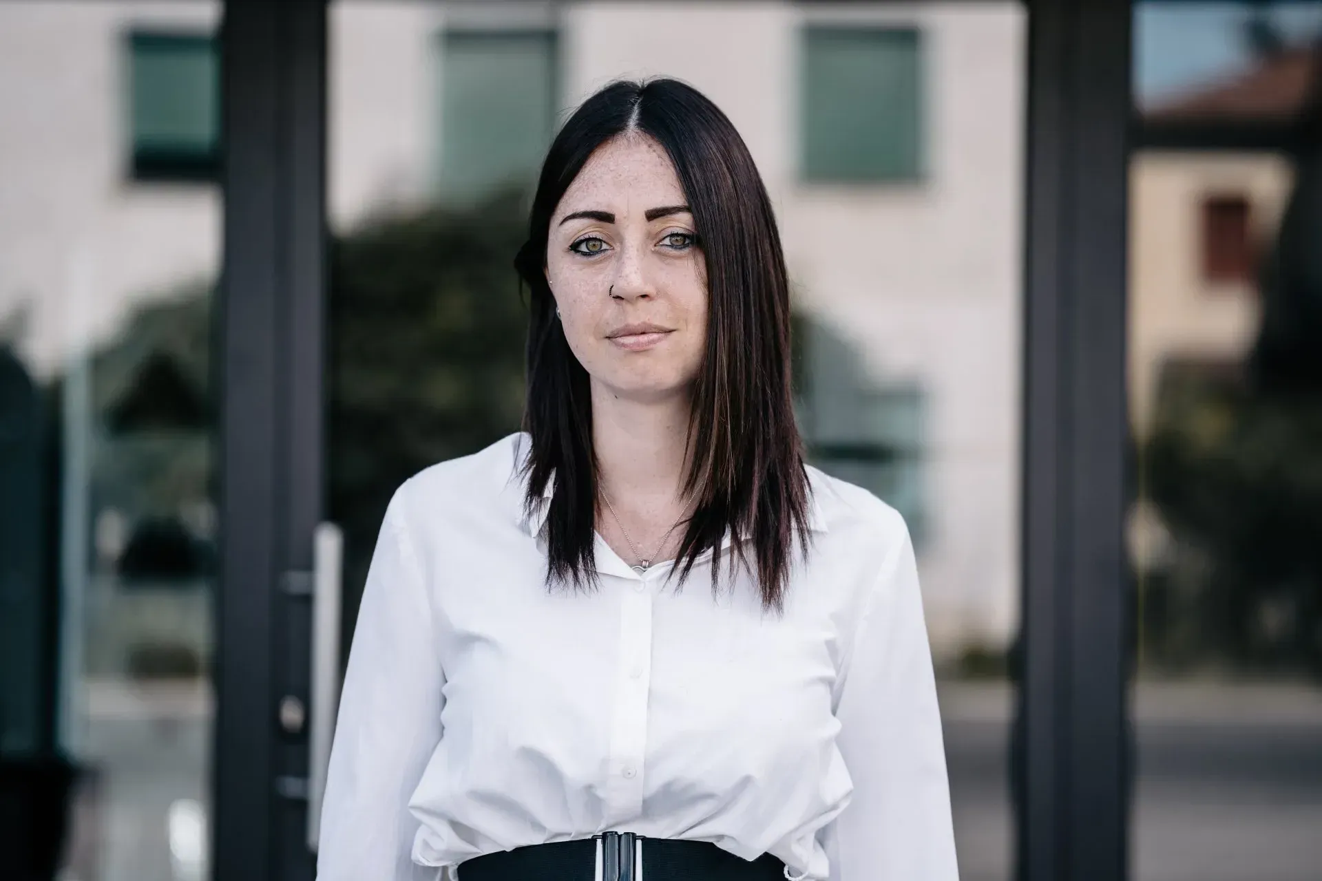 Una donna con una camicia bianca e una gonna nera è in piedi davanti a un edificio.
