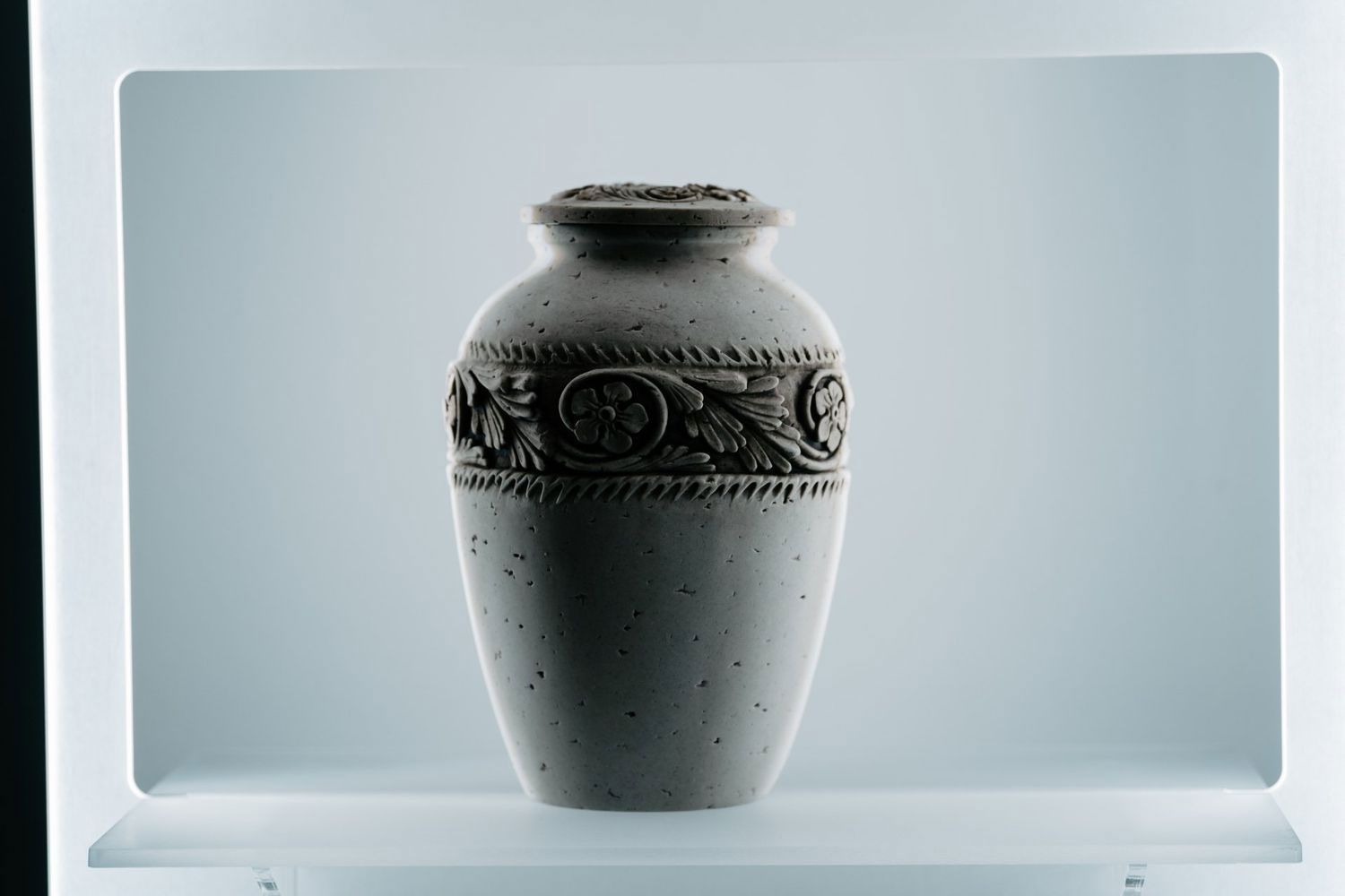 Un vaso bianco è appoggiato su uno scaffale bianco.