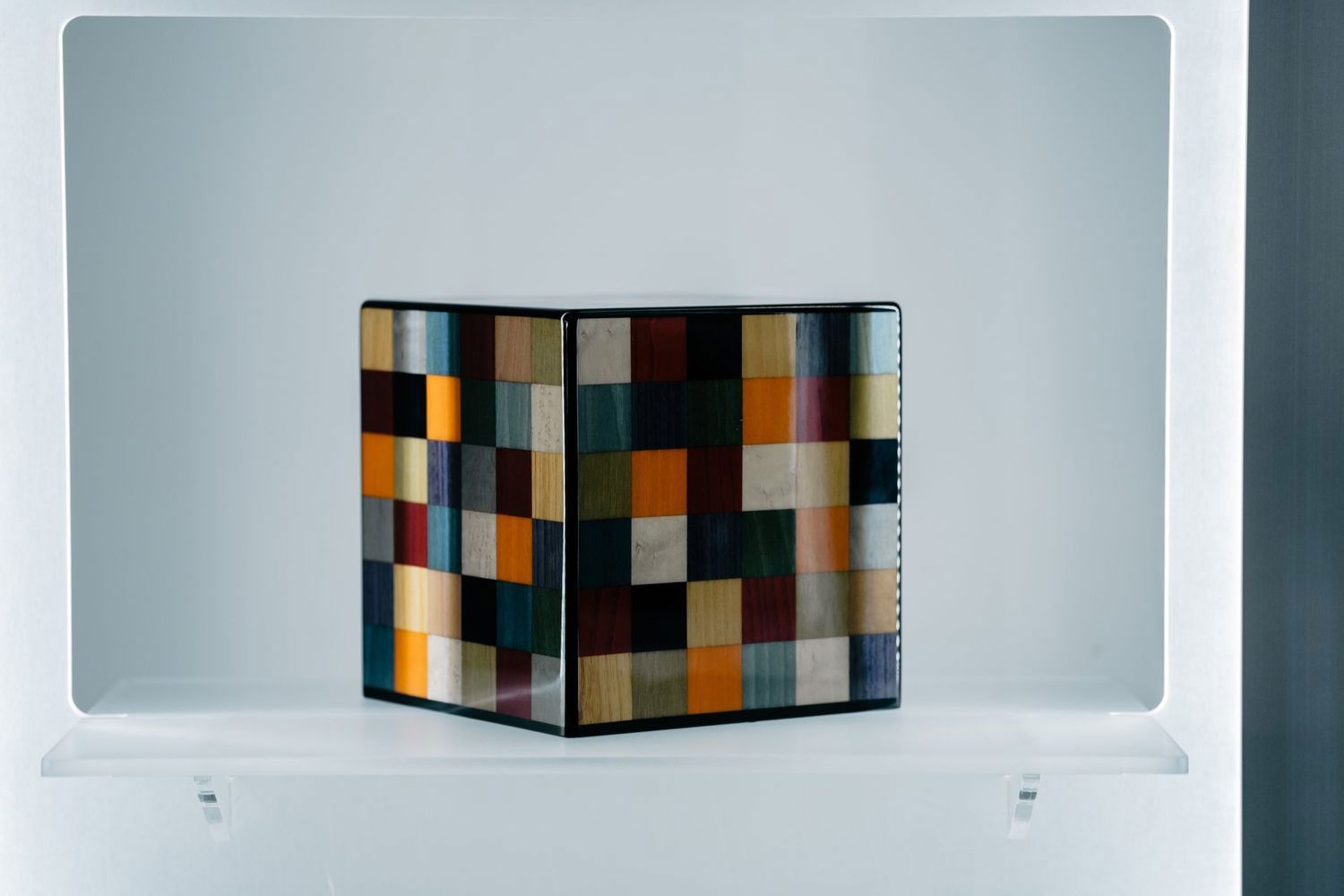 Un cubo colorato è appoggiato su uno scaffale bianco.