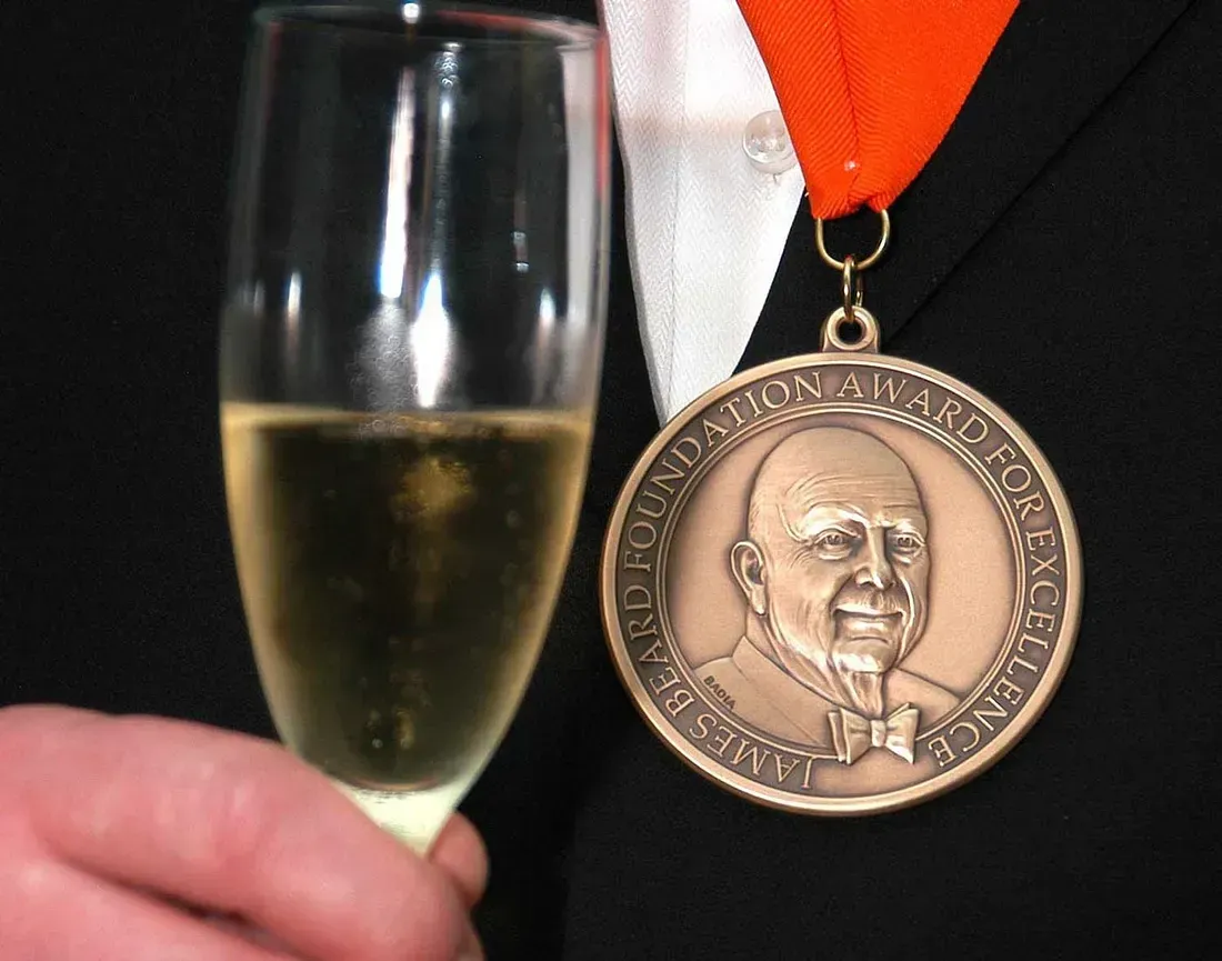 Person wearing a medal, holding champagne flute. Medal says 