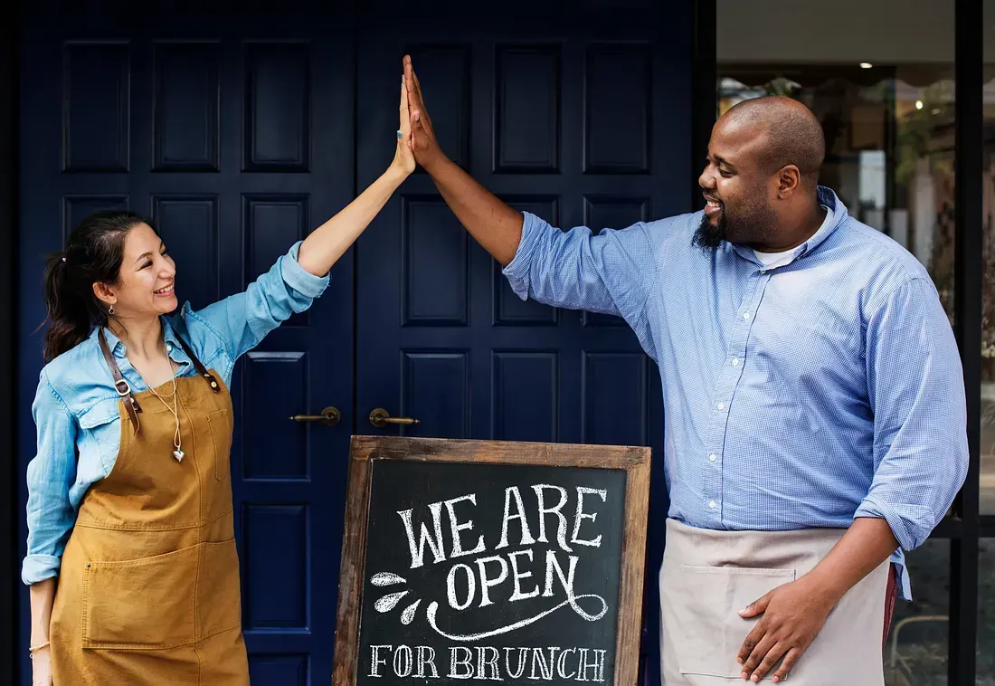 Two people in aprons high-fiving in front of a blue door and 