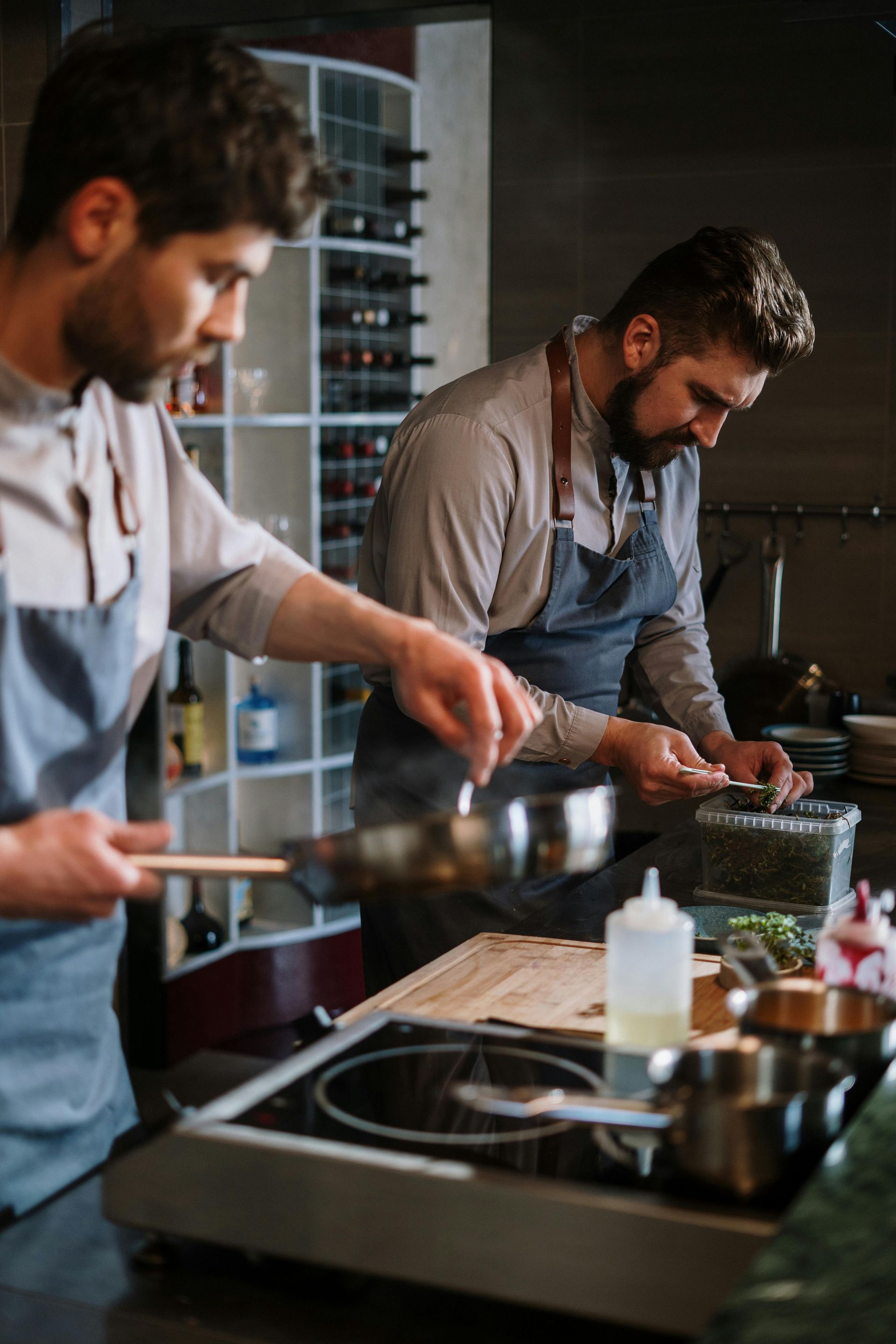 Chefs working in a busy commercial kitchen, cooking on the stove with steam rising.