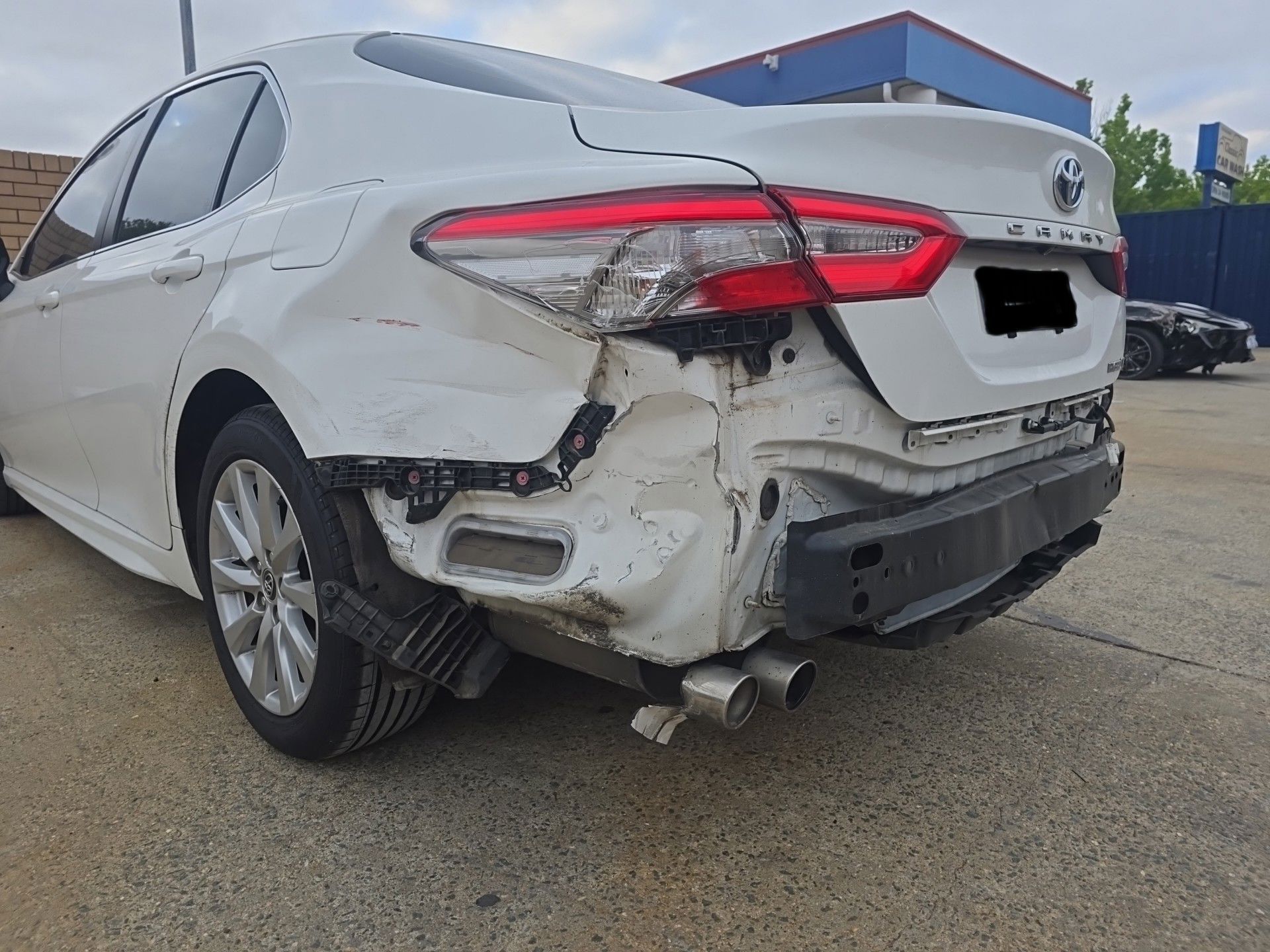 A white car with a damaged bumper is parked in a parking lot — Southside Bodyworks in Greenway, ACT