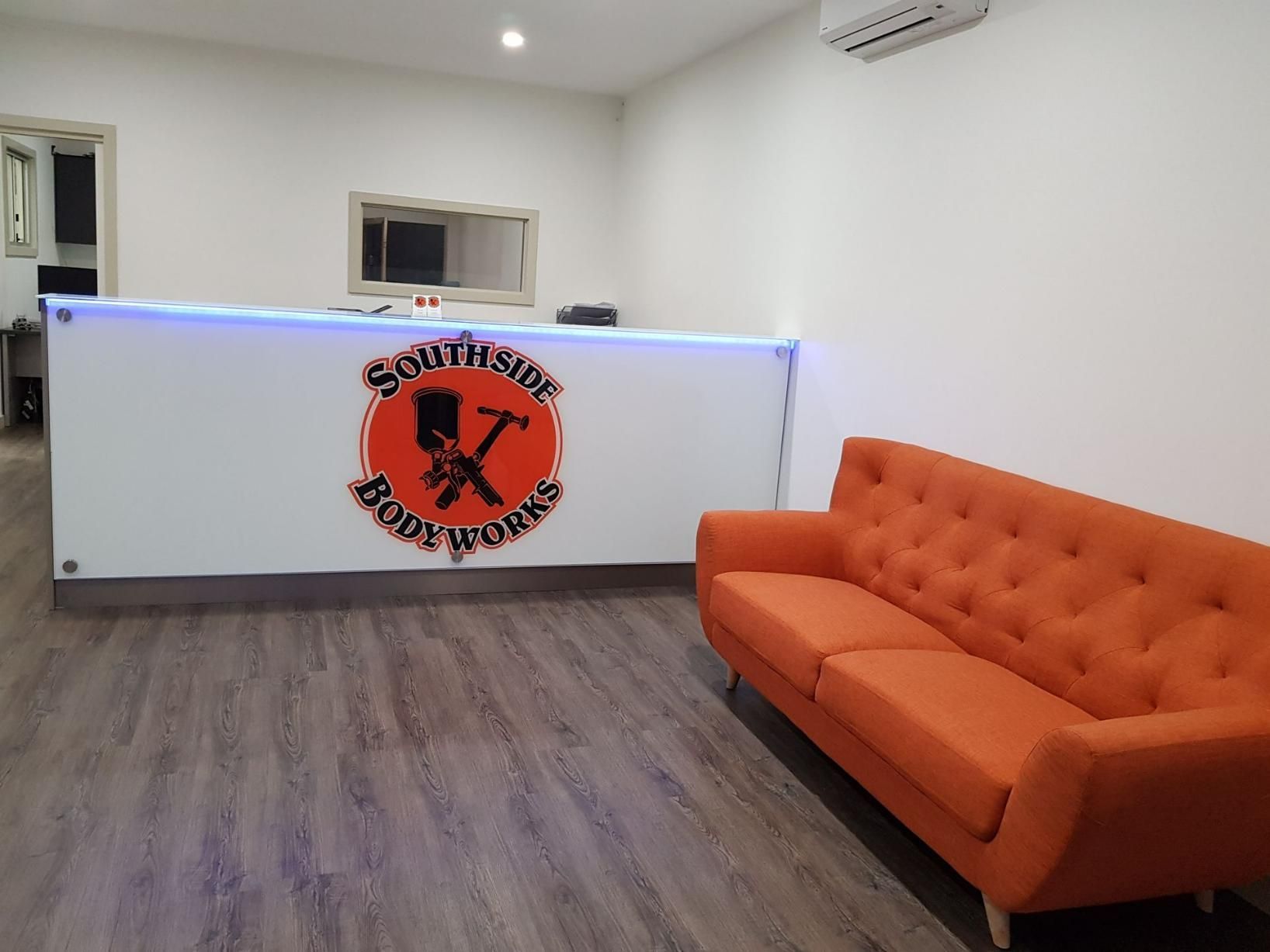 An Orange Couch Is Sitting in Front of A White Counter with A Logo on It — Southside Bodyworks in Greenway, ACT