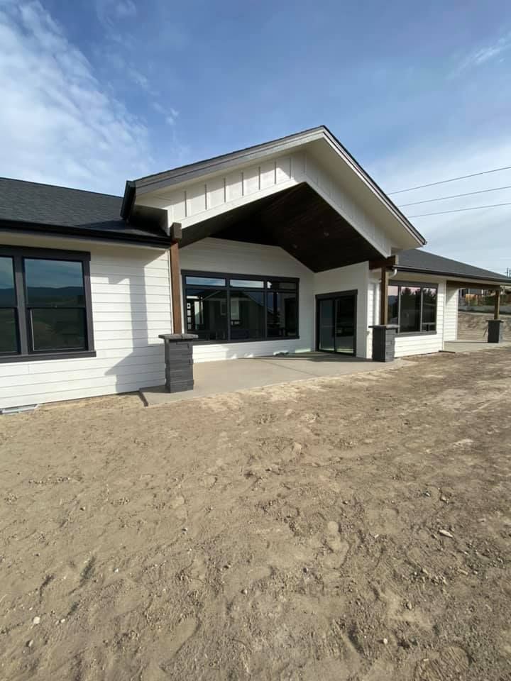 A large white house with a black roof is sitting on top of a dirt field.