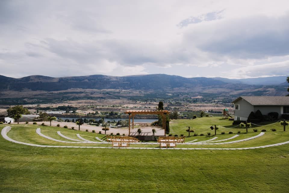 A large grassy field with a house in the background and mountains in the background.
