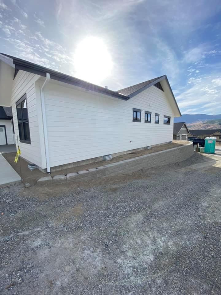 A white house with a black roof is sitting on top of a gravel hill.