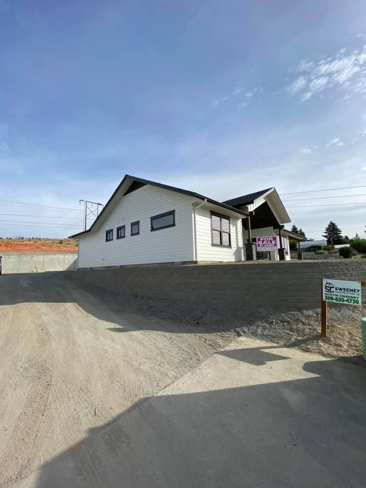 A white house with a black roof is sitting on top of a dirt road.