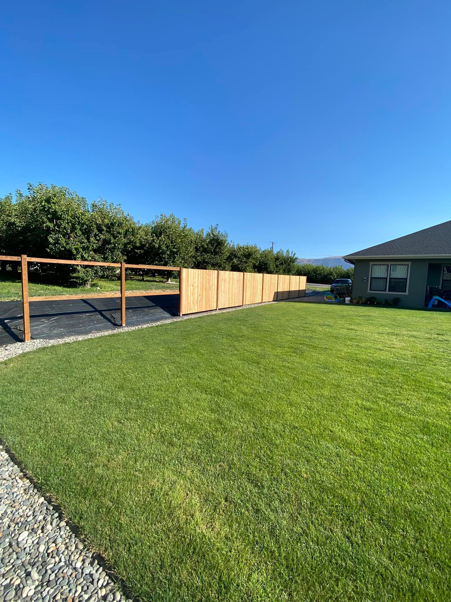 A wooden fence surrounds a lush green lawn in front of a house.