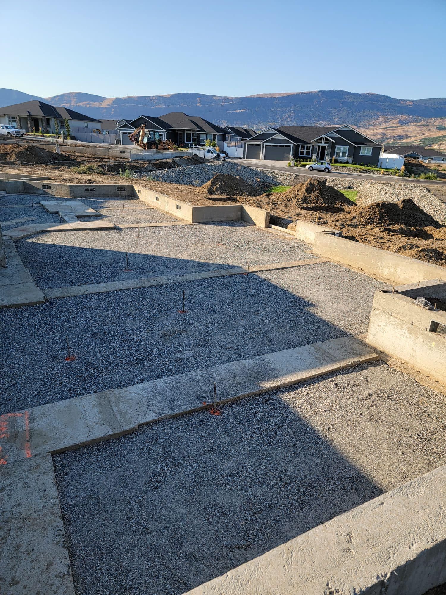 A construction site with a lot of gravel and houses in the background.