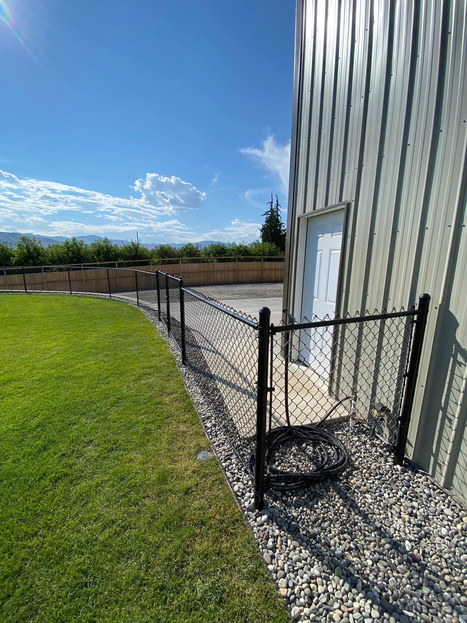 A black chain link fence is surrounding a grassy yard next to a building.