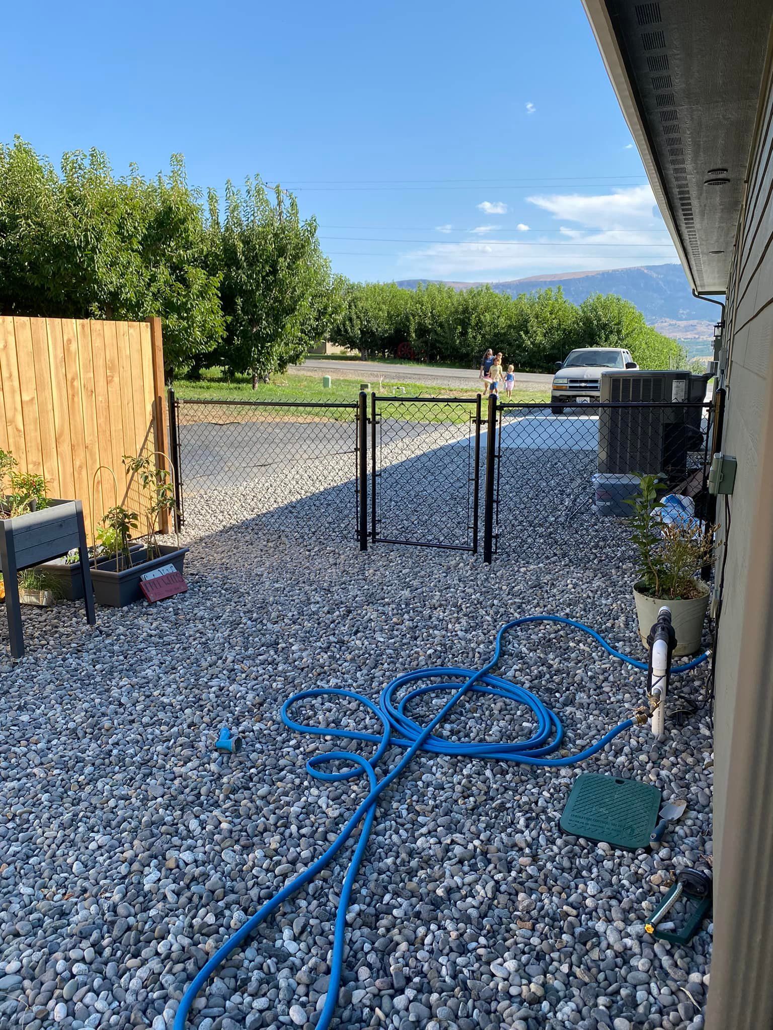 A blue hose is sitting on top of a gravel driveway.