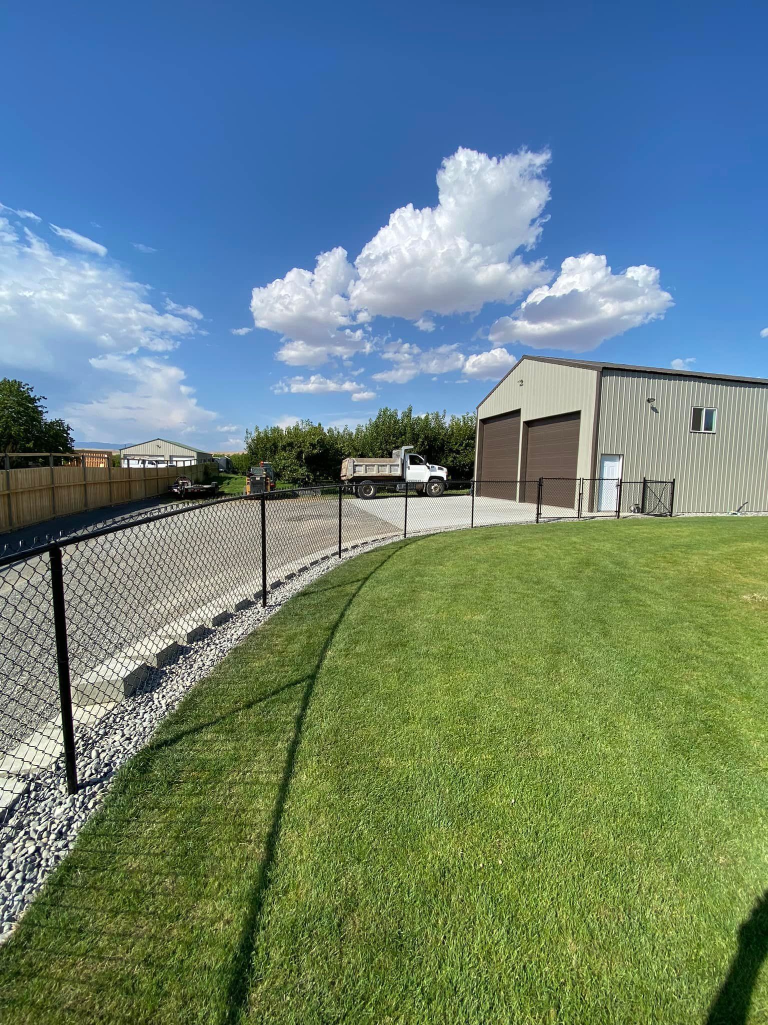 A large grassy field with a fence and a building in the background.
