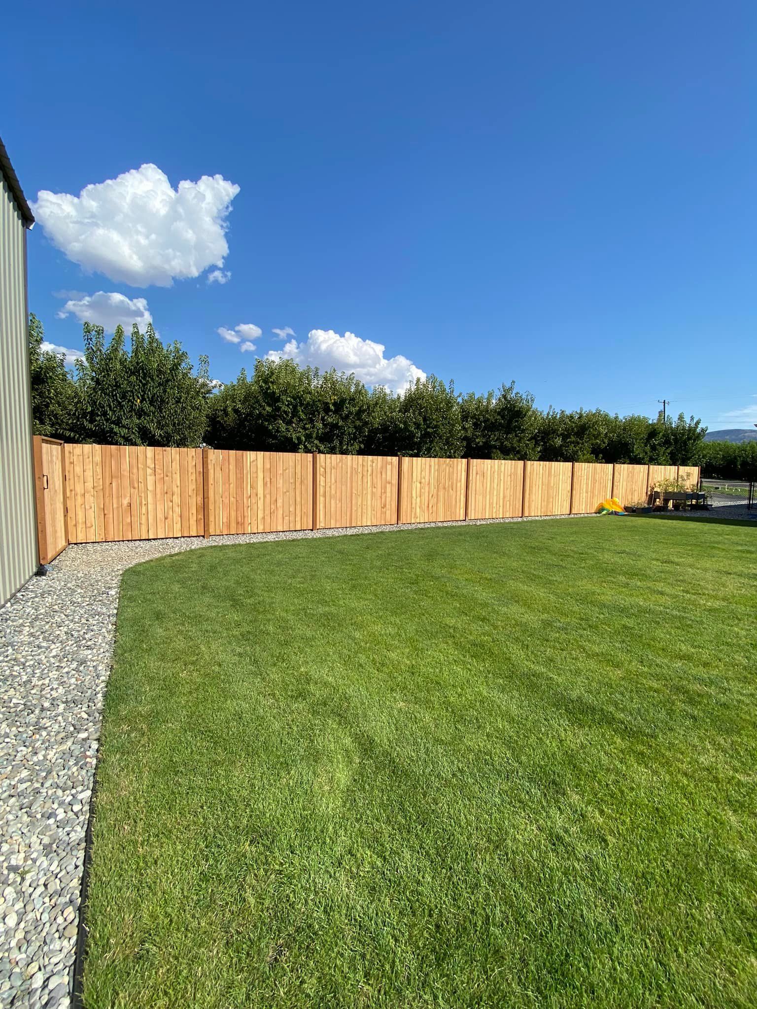 A wooden fence surrounds a lush green lawn in a backyard.