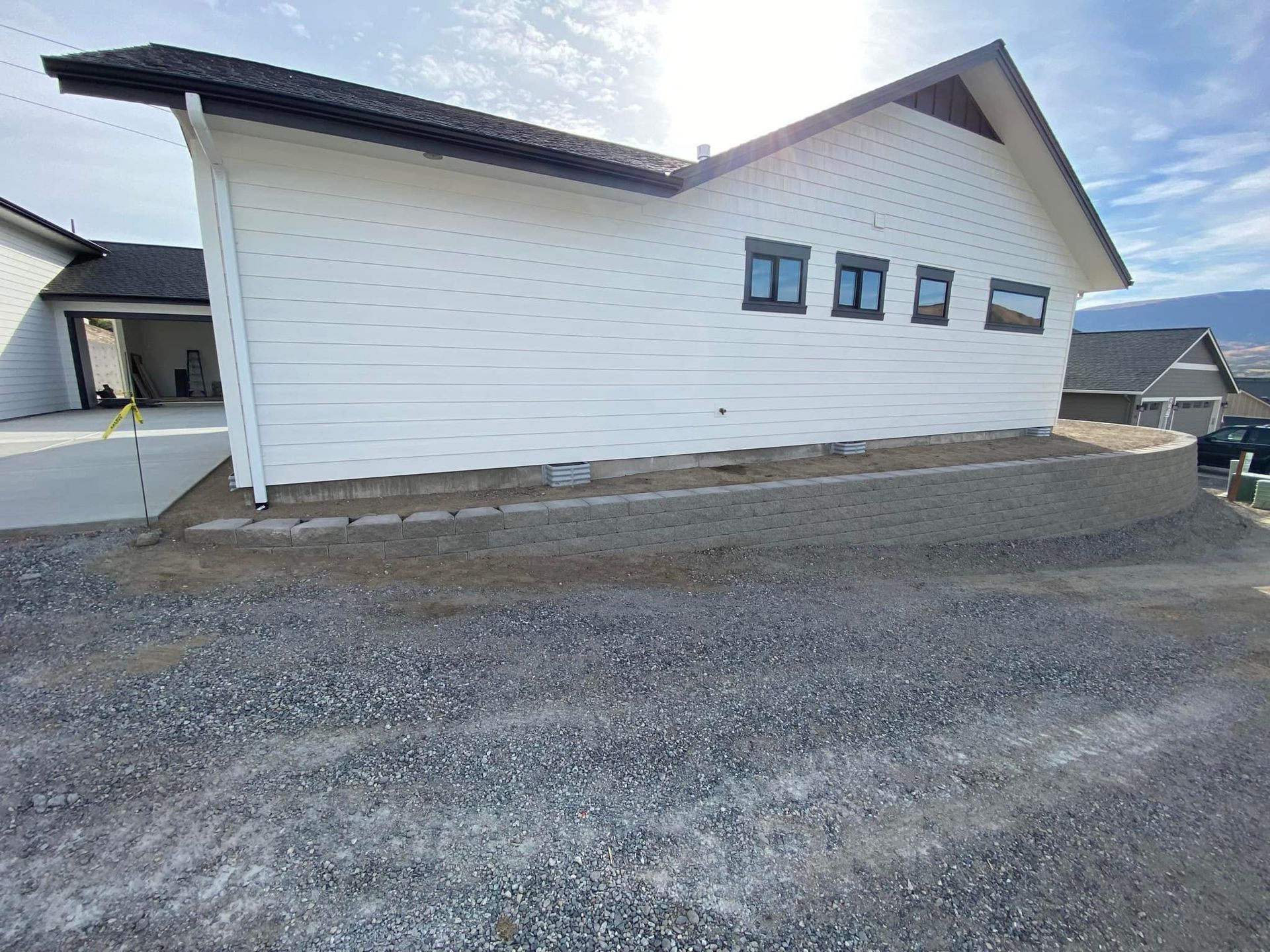 A white house with a black roof is sitting on top of a gravel road.