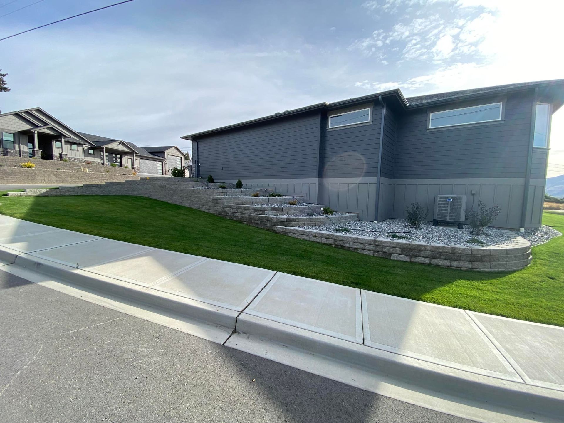 A house is sitting on top of a lush green hill next to a sidewalk.