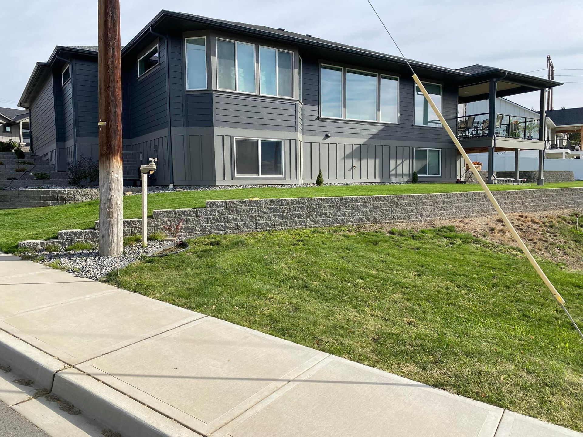 A large house with a lot of windows is sitting on a hill next to a sidewalk.