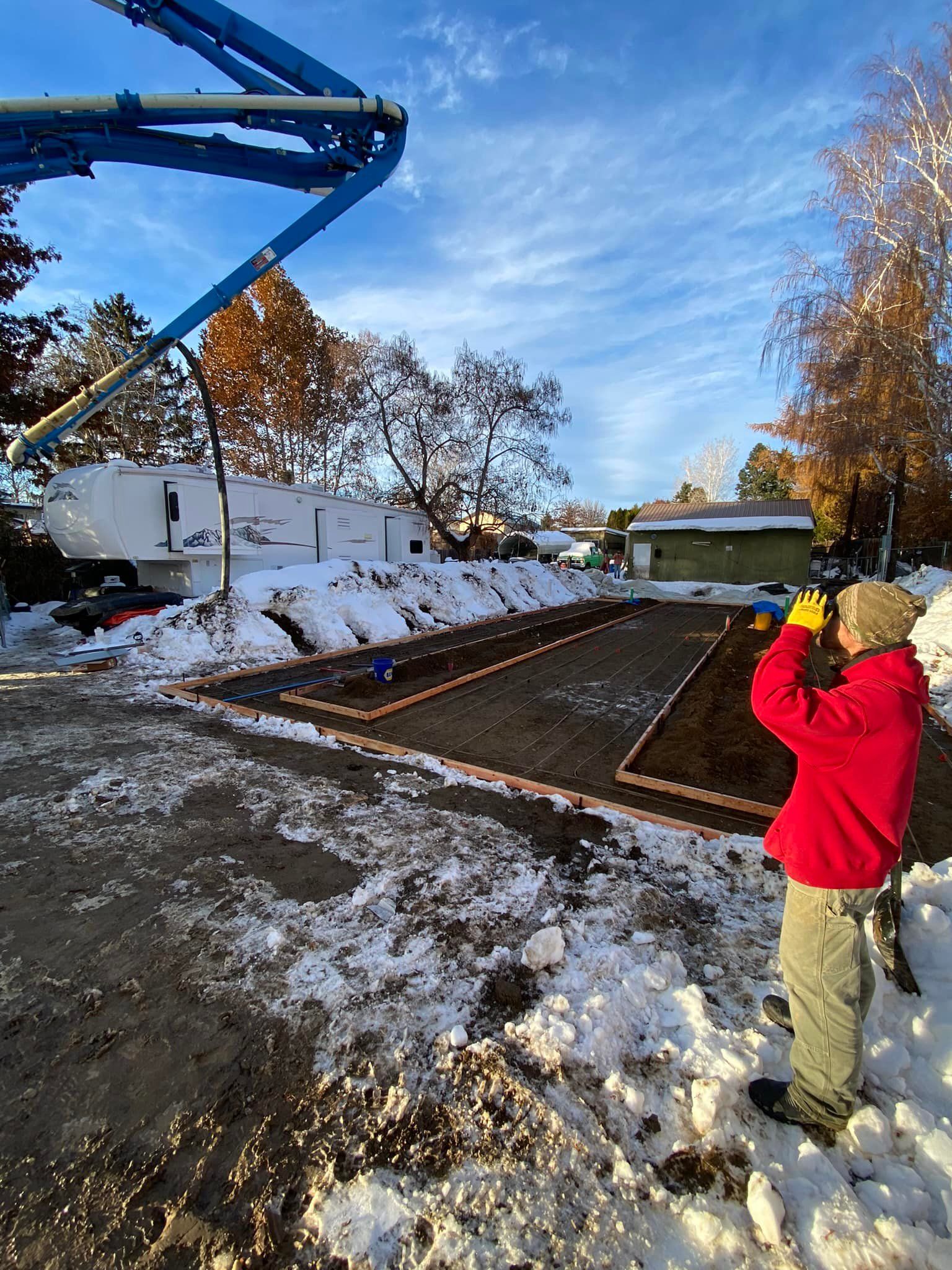 A man in a red jacket is standing in the snow in front of a concrete pump.