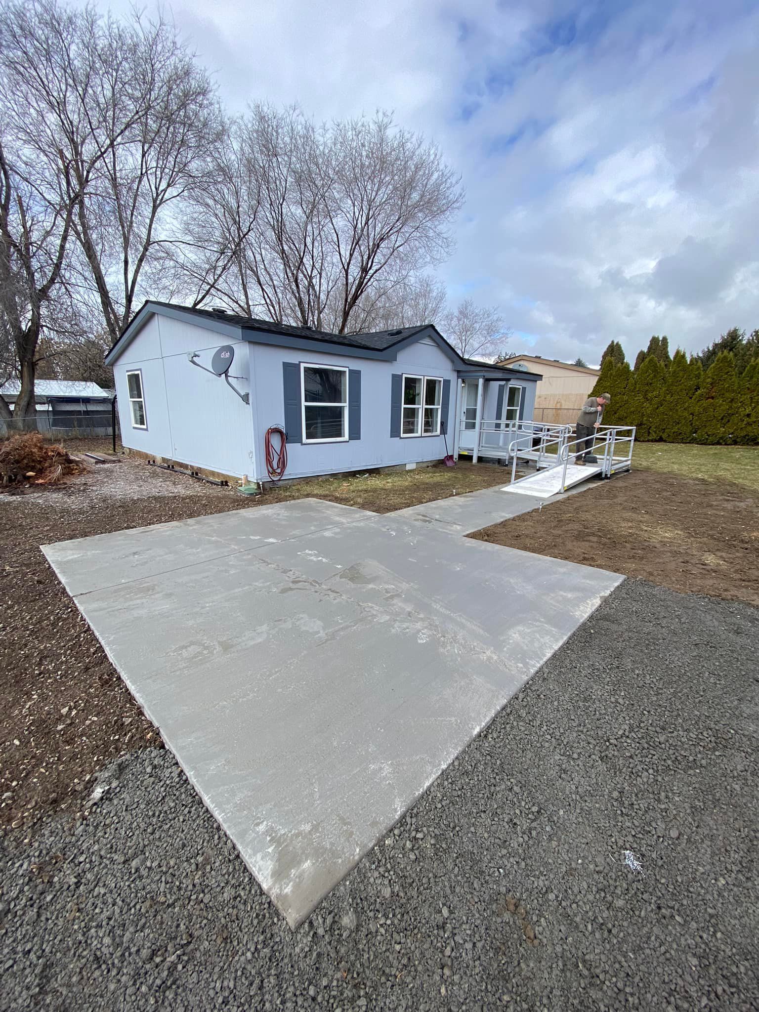 A mobile home is sitting on top of a gravel lot next to a concrete driveway.
