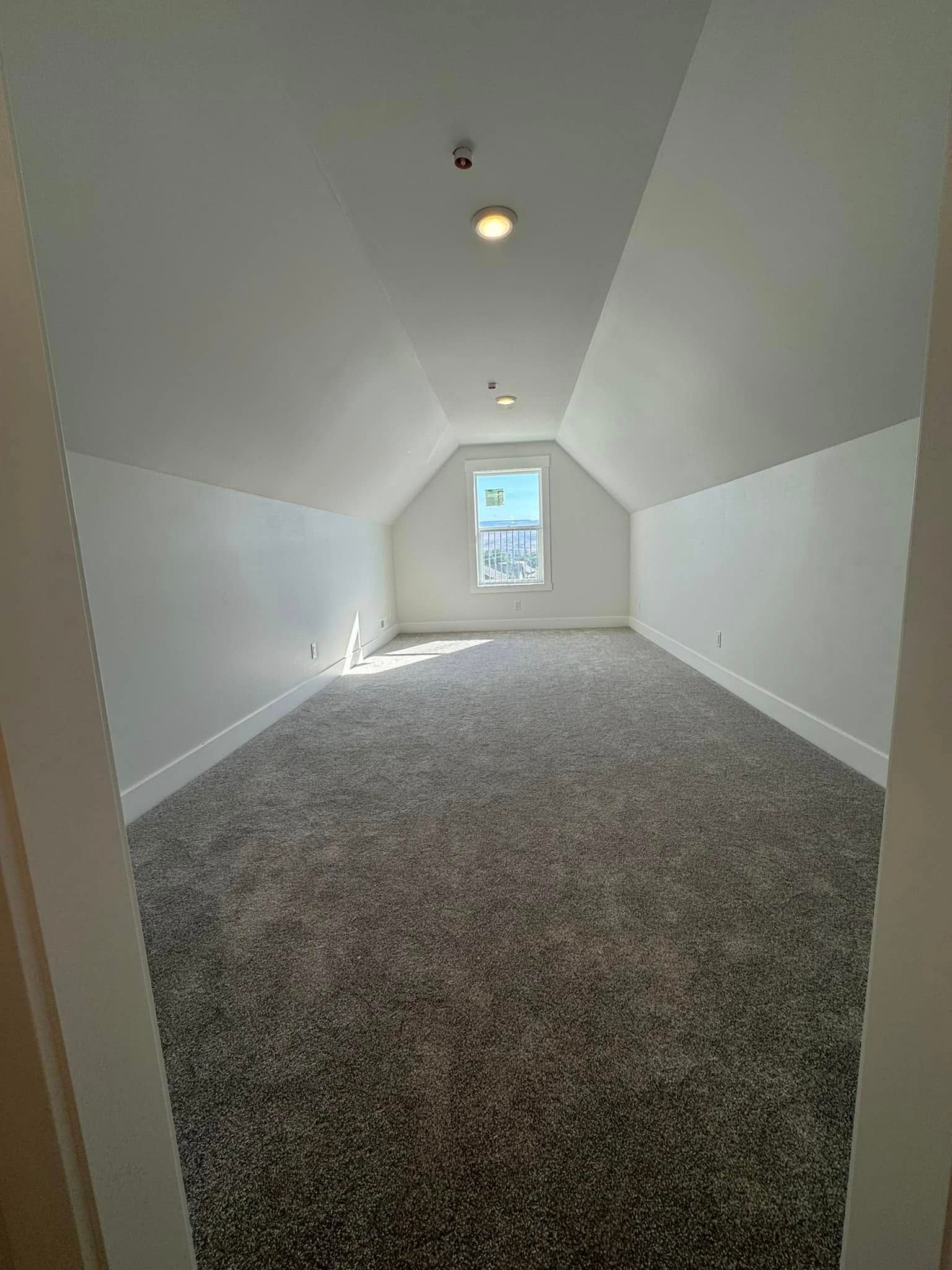 An empty attic with a vaulted ceiling and a window.