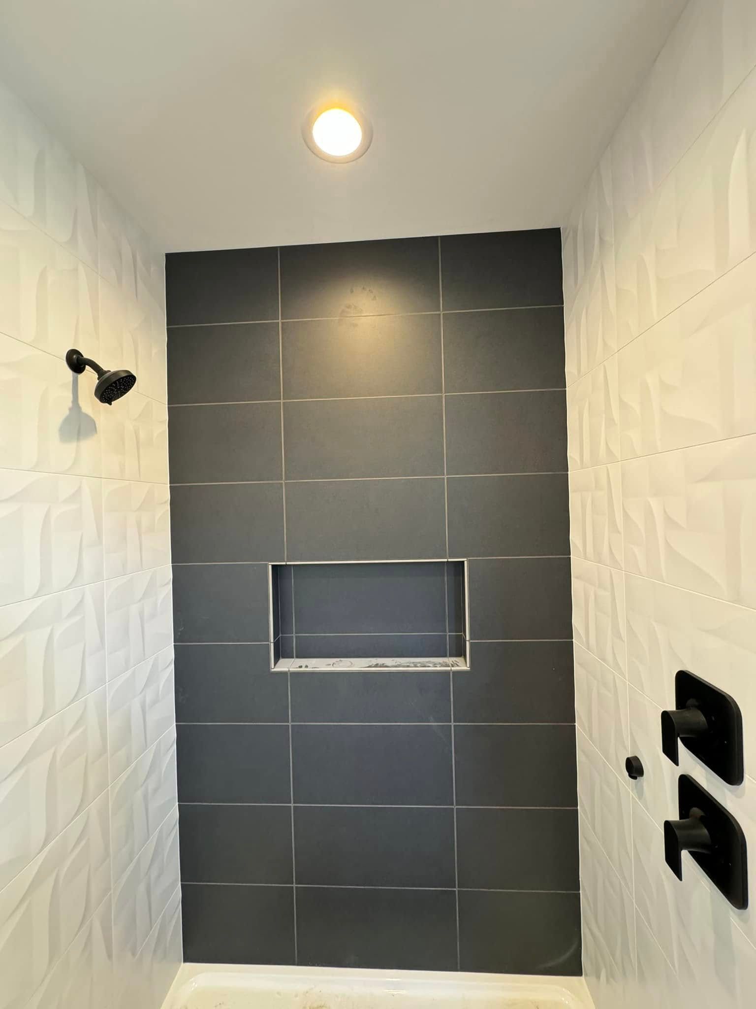 A shower with black tiles and a niche in the wall.