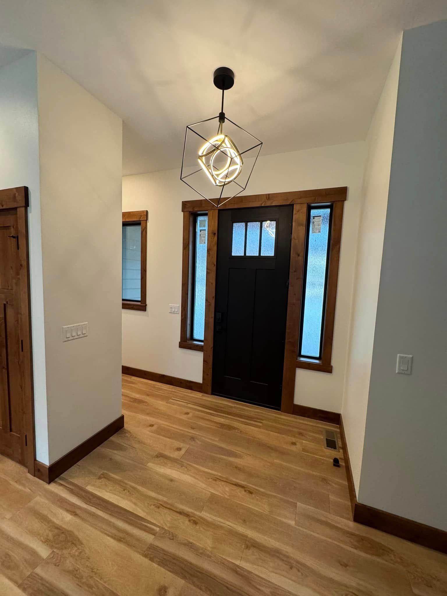 A hallway with hardwood floors and a black door in a house.