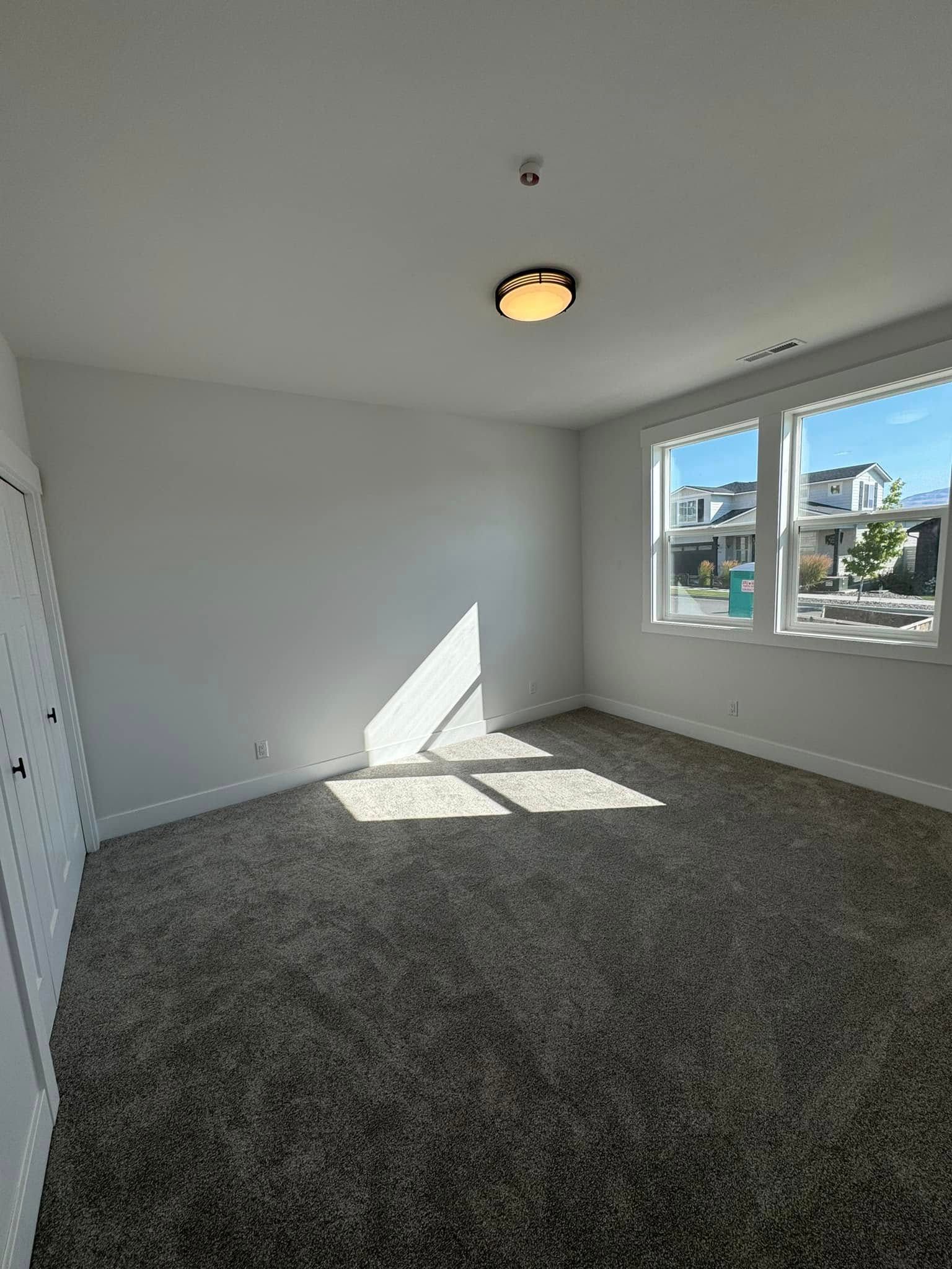 An empty bedroom with a carpeted floor and two windows.