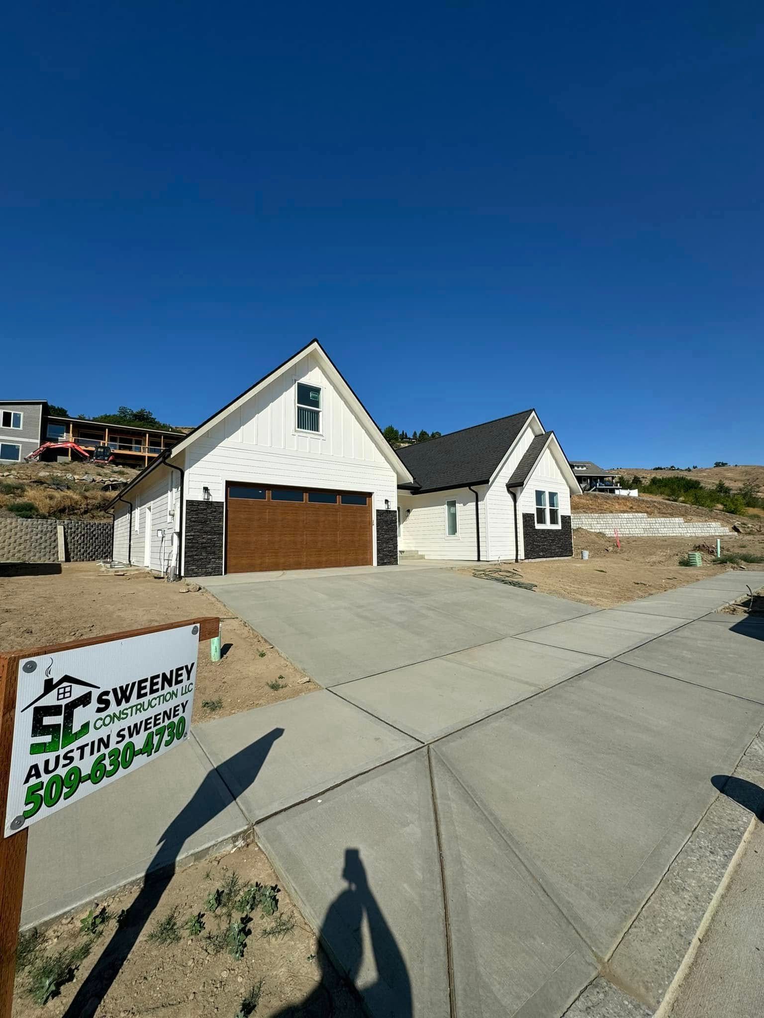 A white house with a brown garage door and a sign in front of it.