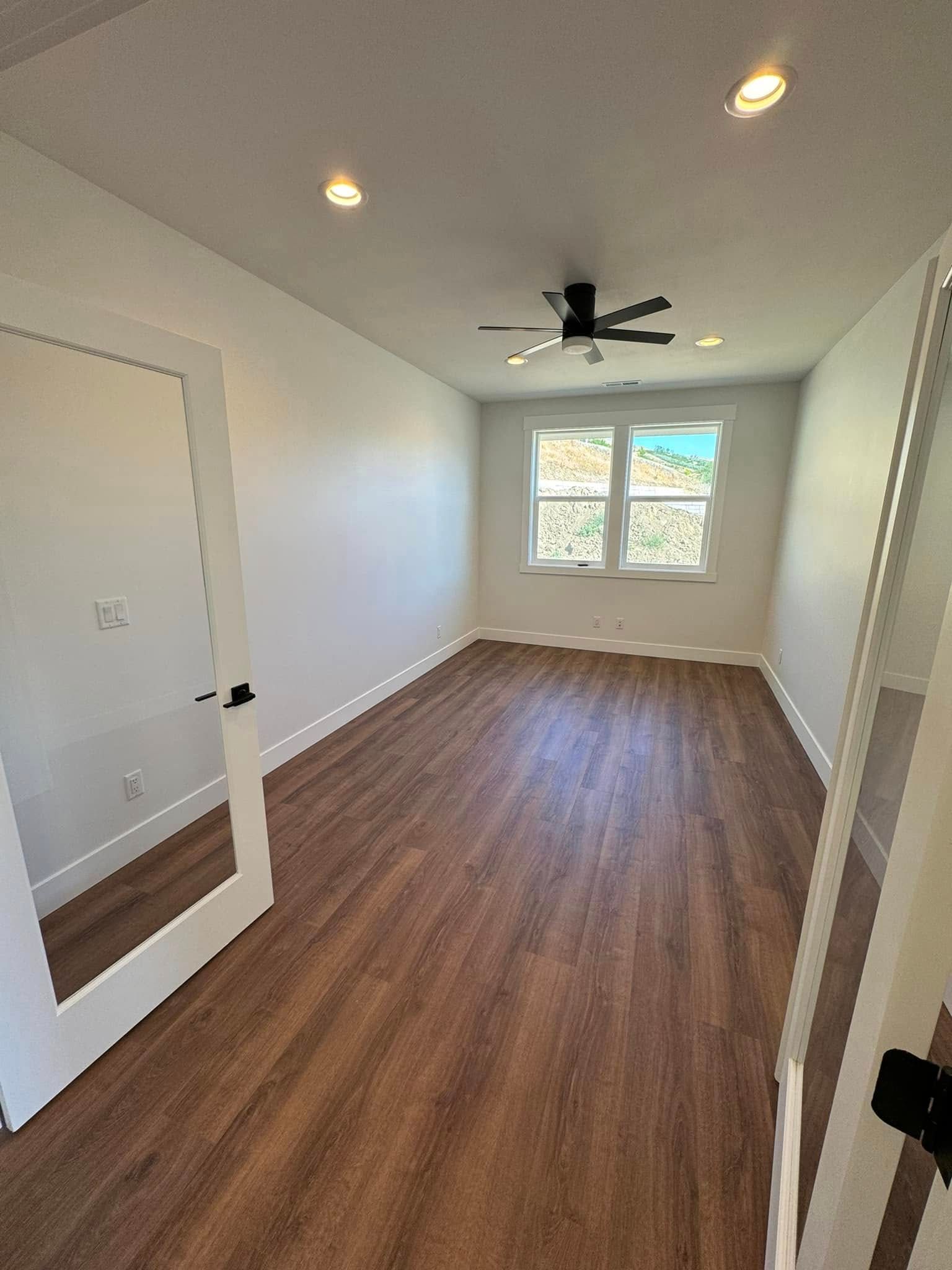 A bedroom with hardwood floors , a ceiling fan and a mirror.