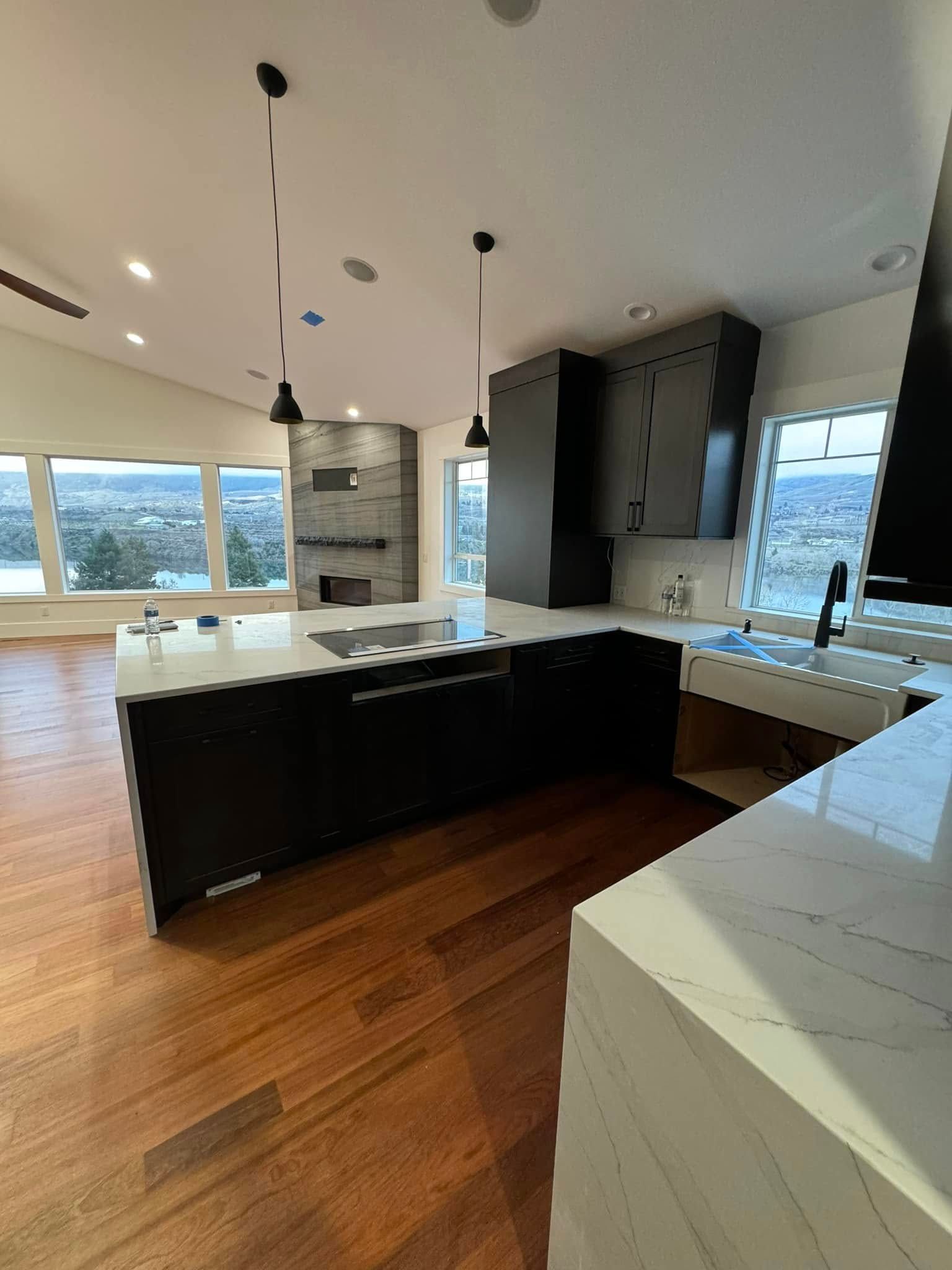 A kitchen with black cabinets , white counter tops , and hardwood floors.