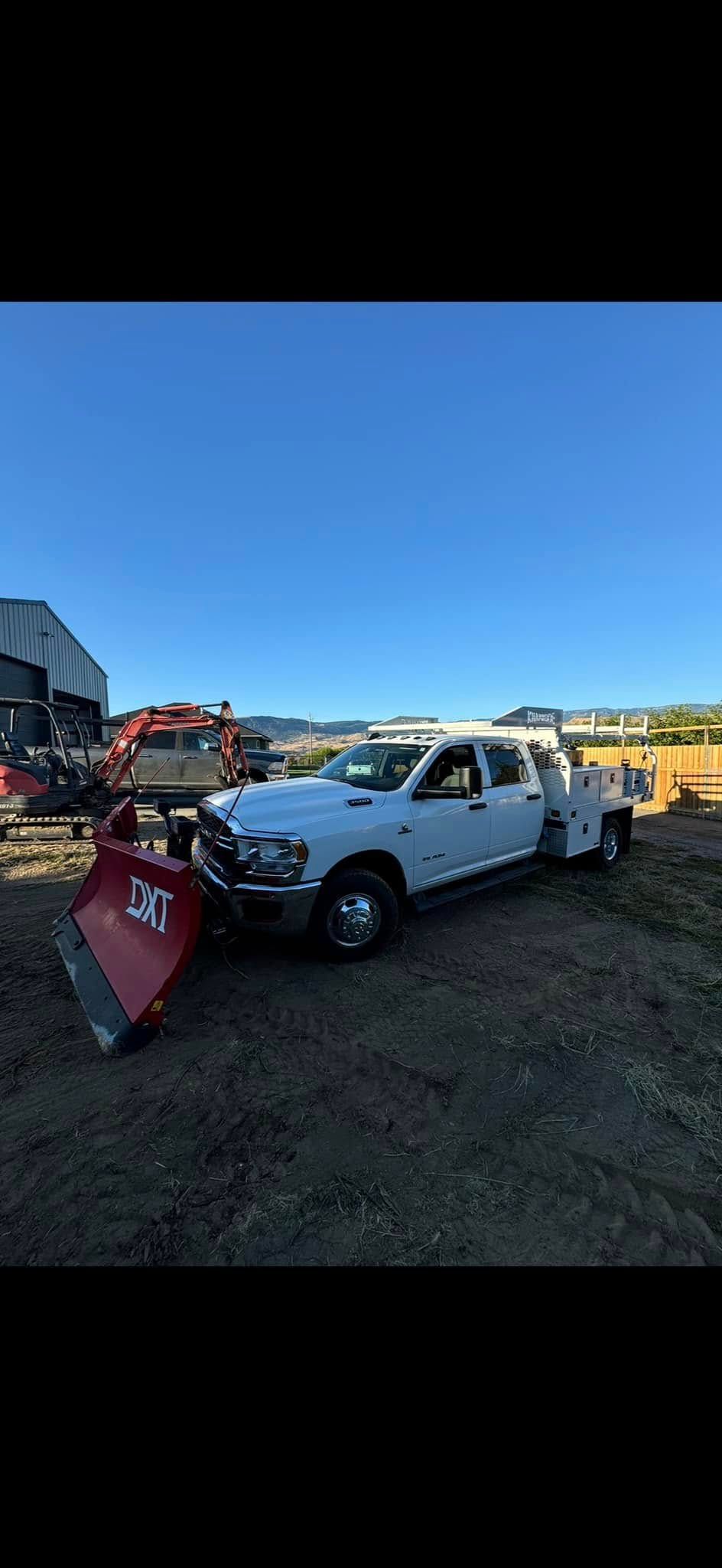 A white truck with a snow plow attached to it is parked in a field.