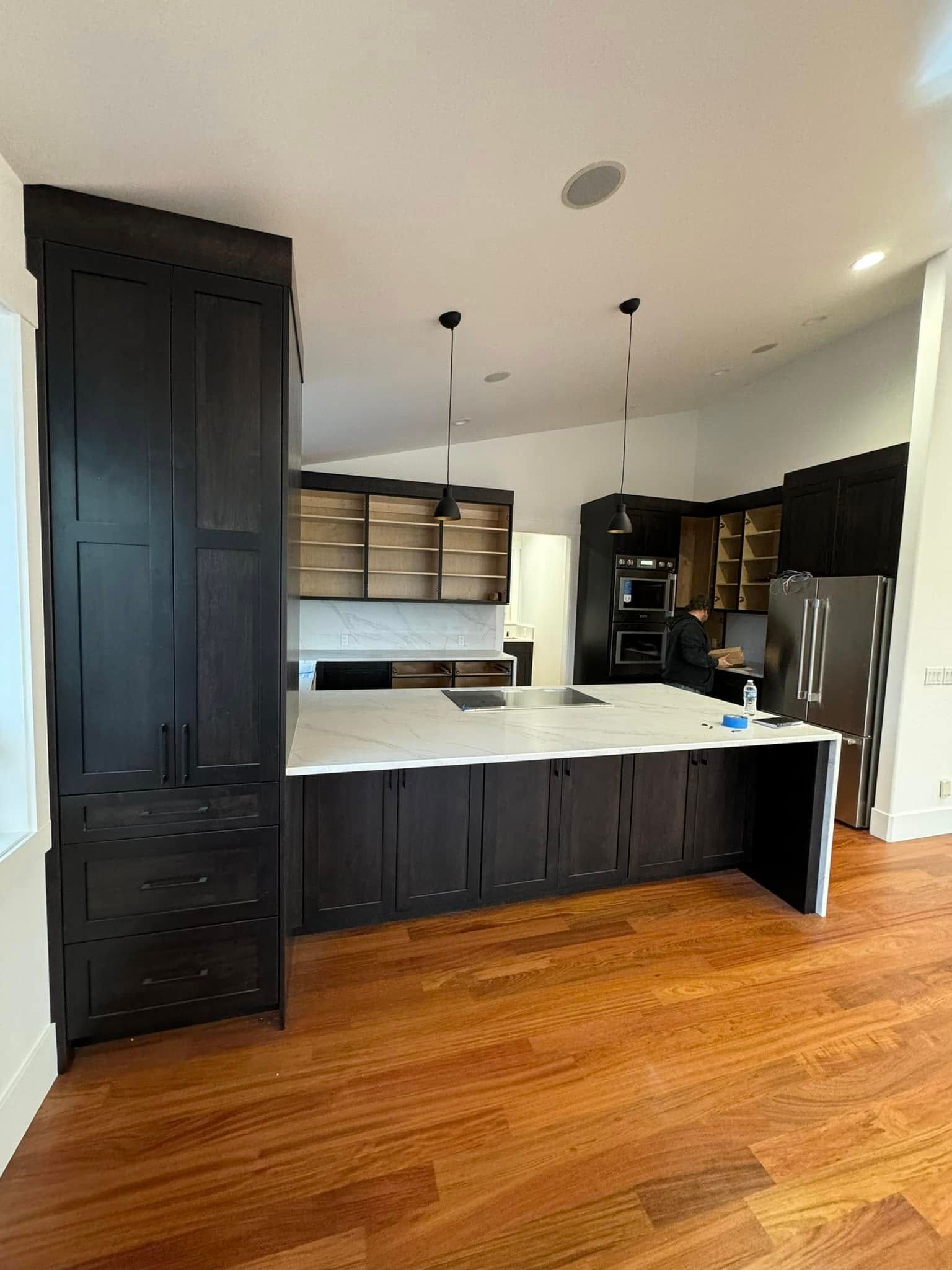 A kitchen with black cabinets , white counter tops , and hardwood floors.