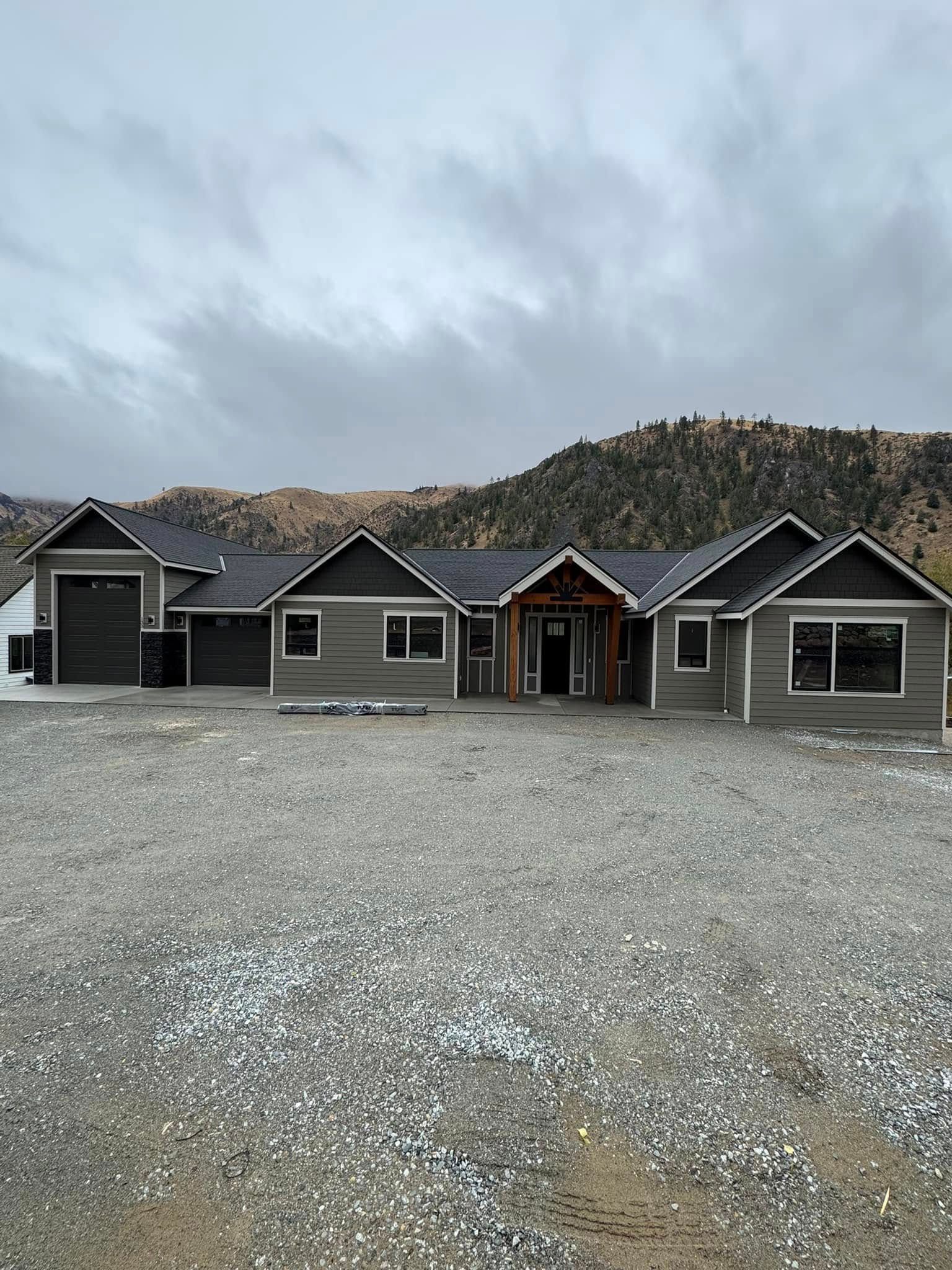 A large house is sitting on top of a gravel lot with mountains in the background.