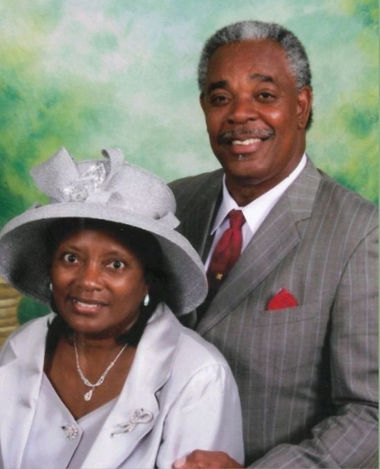 A man in a suit and tie stands next to a woman in a hat