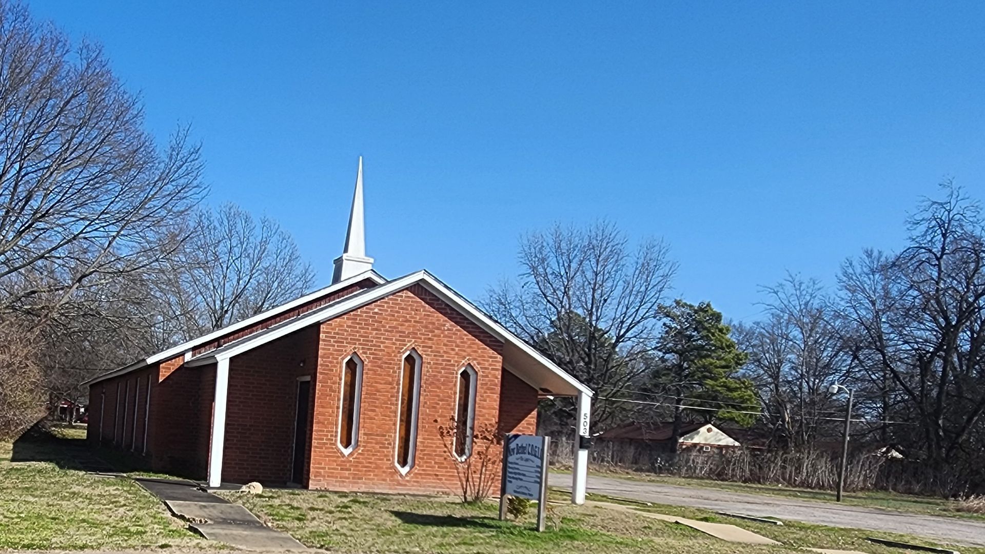 A small brick church with a steeple and a sign in front of it