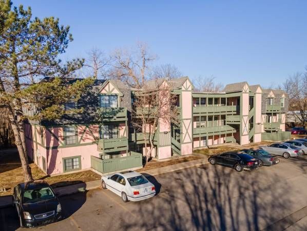 Pink and green multi-story apartment building with parking; cars are parked in front.