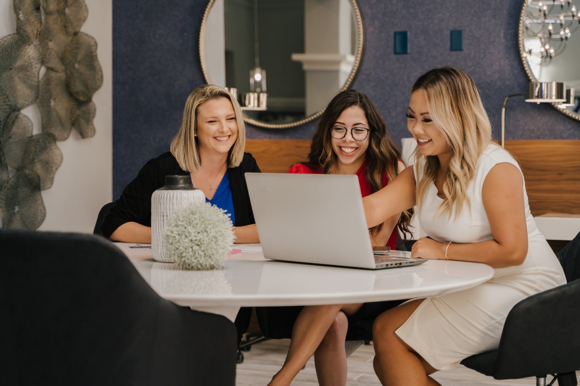 Three women are sitting at a table looking at a laptop computer.