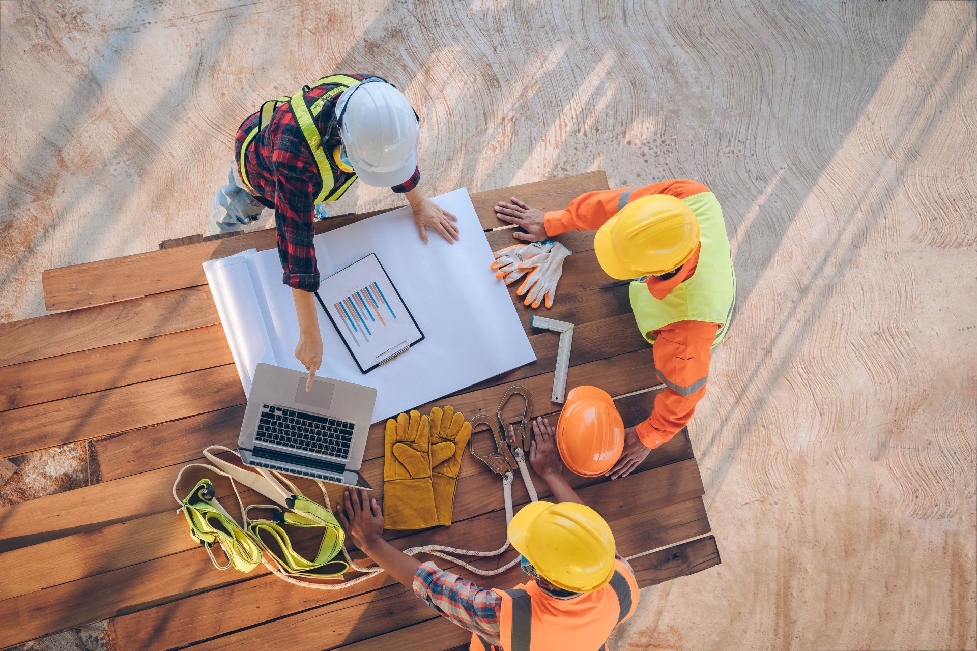 A group of construction workers are sitting around a wooden table looking at a blueprint.